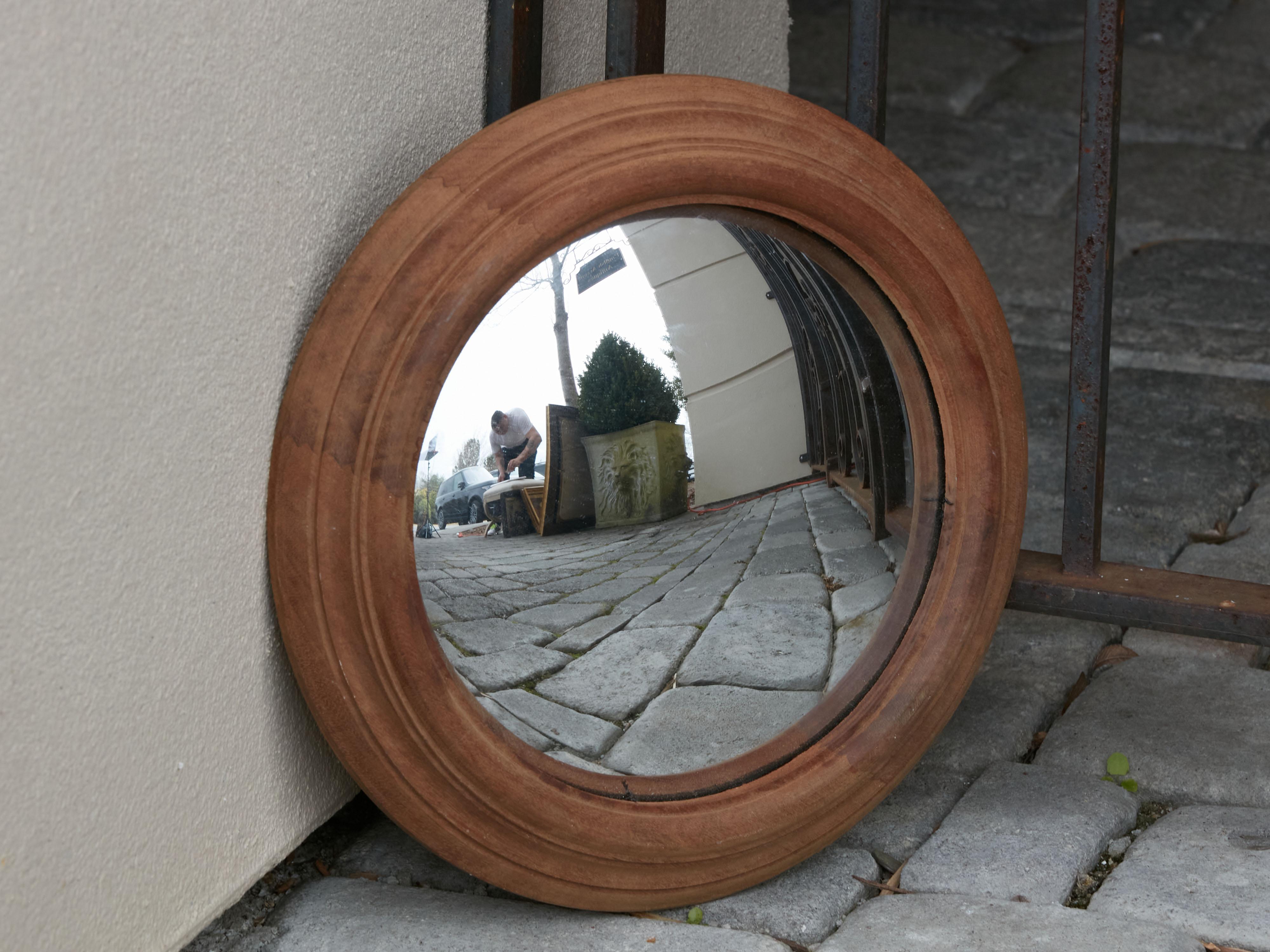 An English convex bullseye mirror with molded frame. Created in England, this wall mirror features a simple circular frame with molded accents, surrounding a convex mirror sought after for its distorted reflection. An elegant addition to any home,