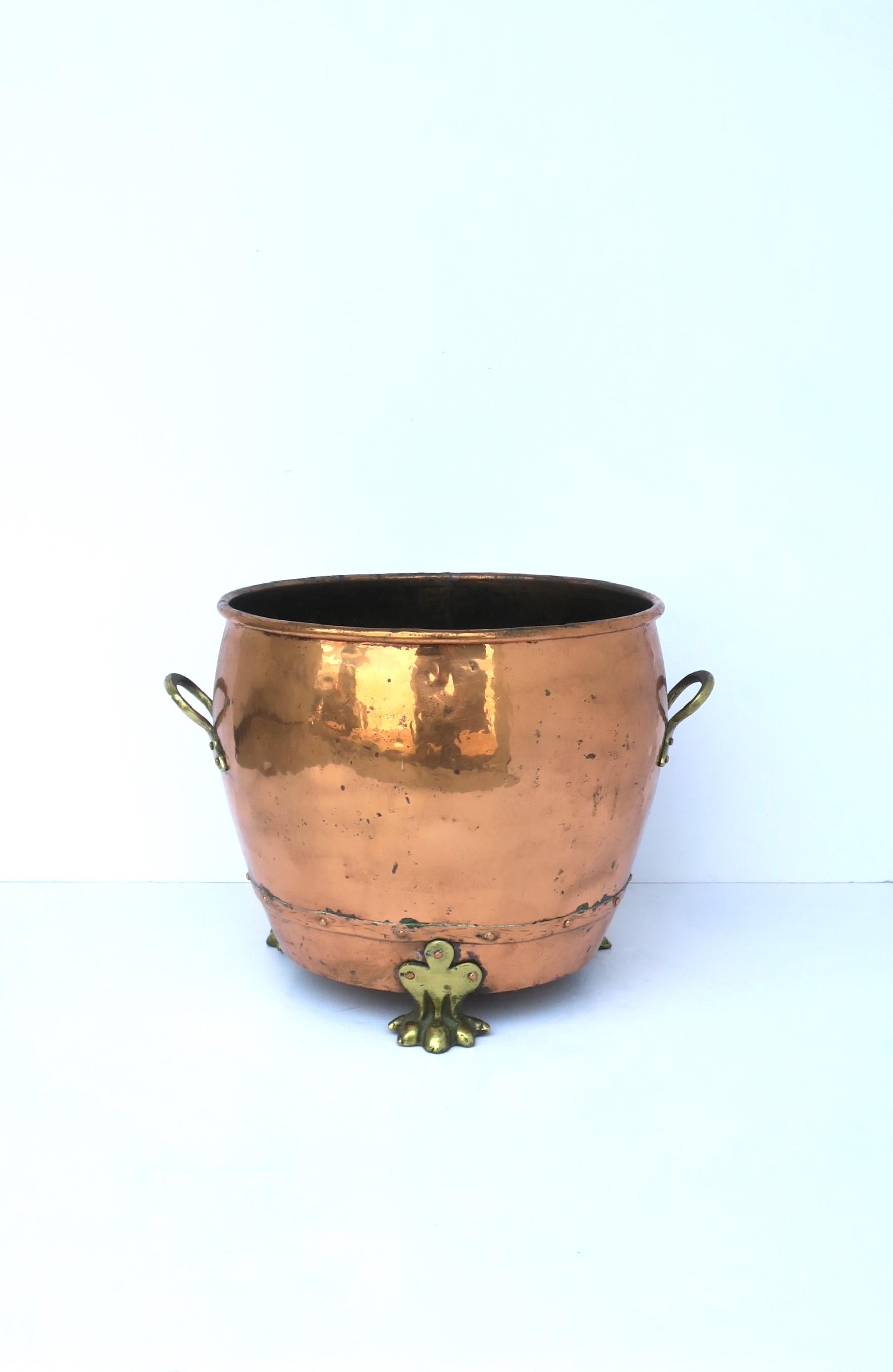 A substantial English fireplace copper and brass chimney or firewood pot with lion paw feet, circa late 19th century to early-20th century, England. Pot is copper with brass handles on either side, brass tri-base lion paw feet, and rivet detail.