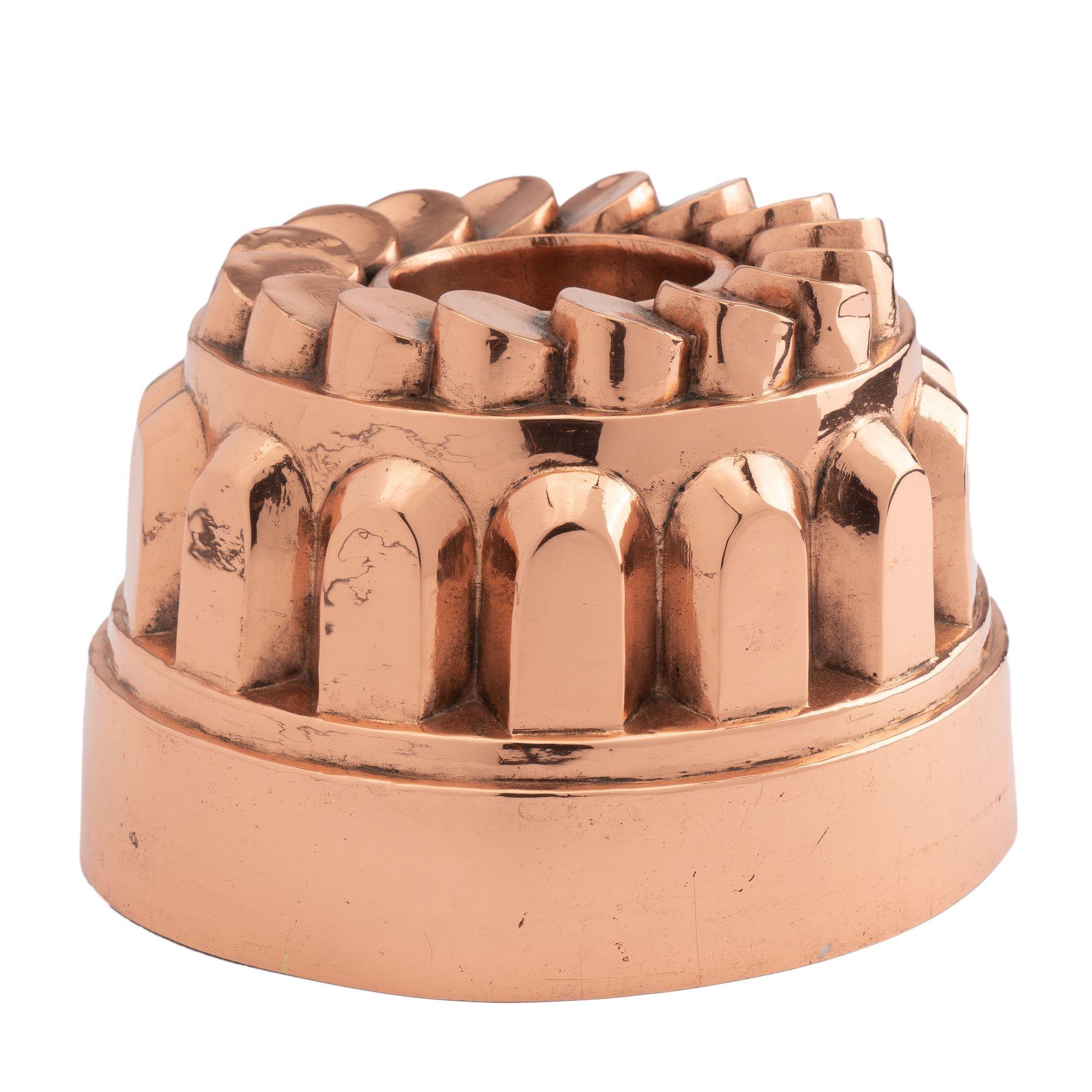 Copper “coin” bundt mold with tin lining. The mold features up-right buttress/turret elements above the deep rim which are capped with overlapping circular 