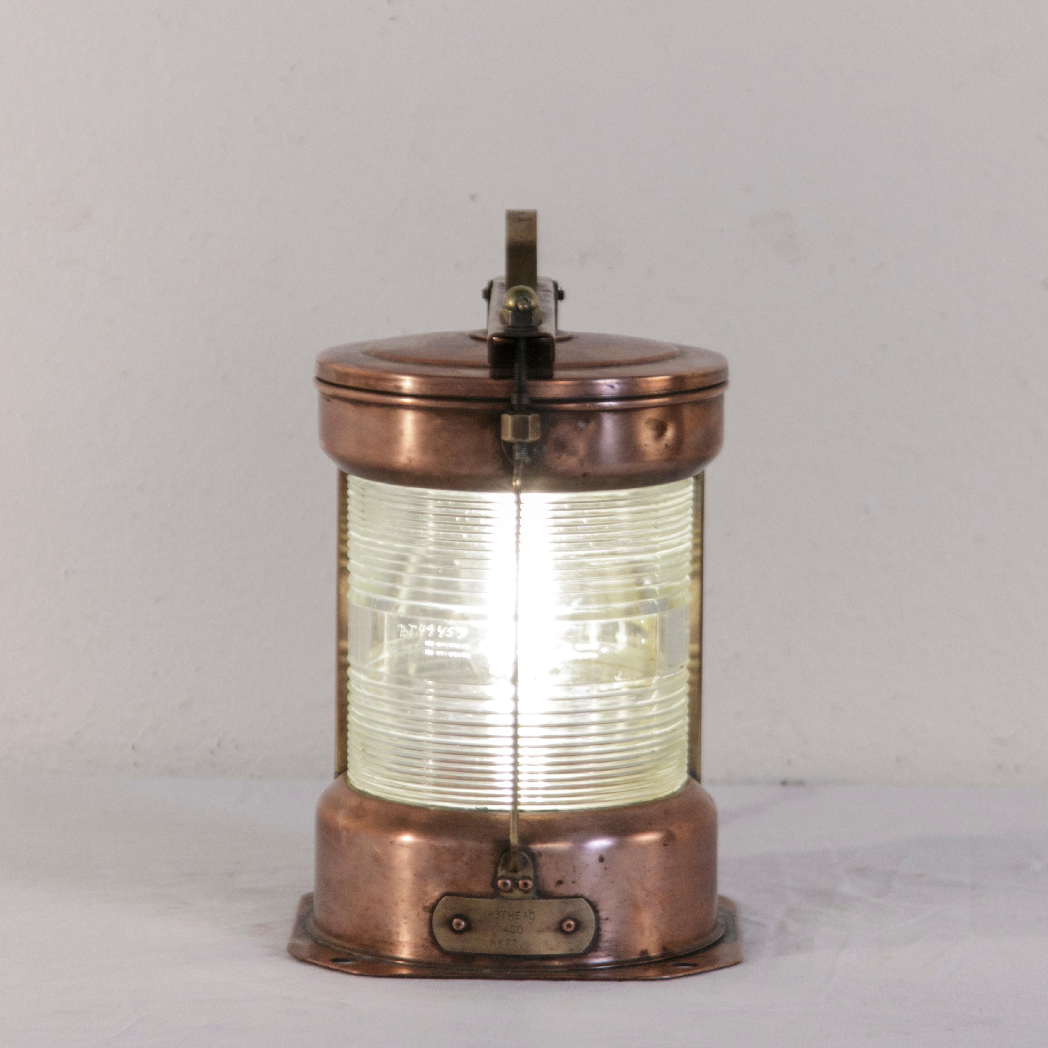 This copper marine lantern from the 20th century features a brass handle and brass label marked Masthead. The original hurricane glass is etched with the serial number BT49459. Converted into a lamp and fitted with a bayonet fit Edison light bulb,