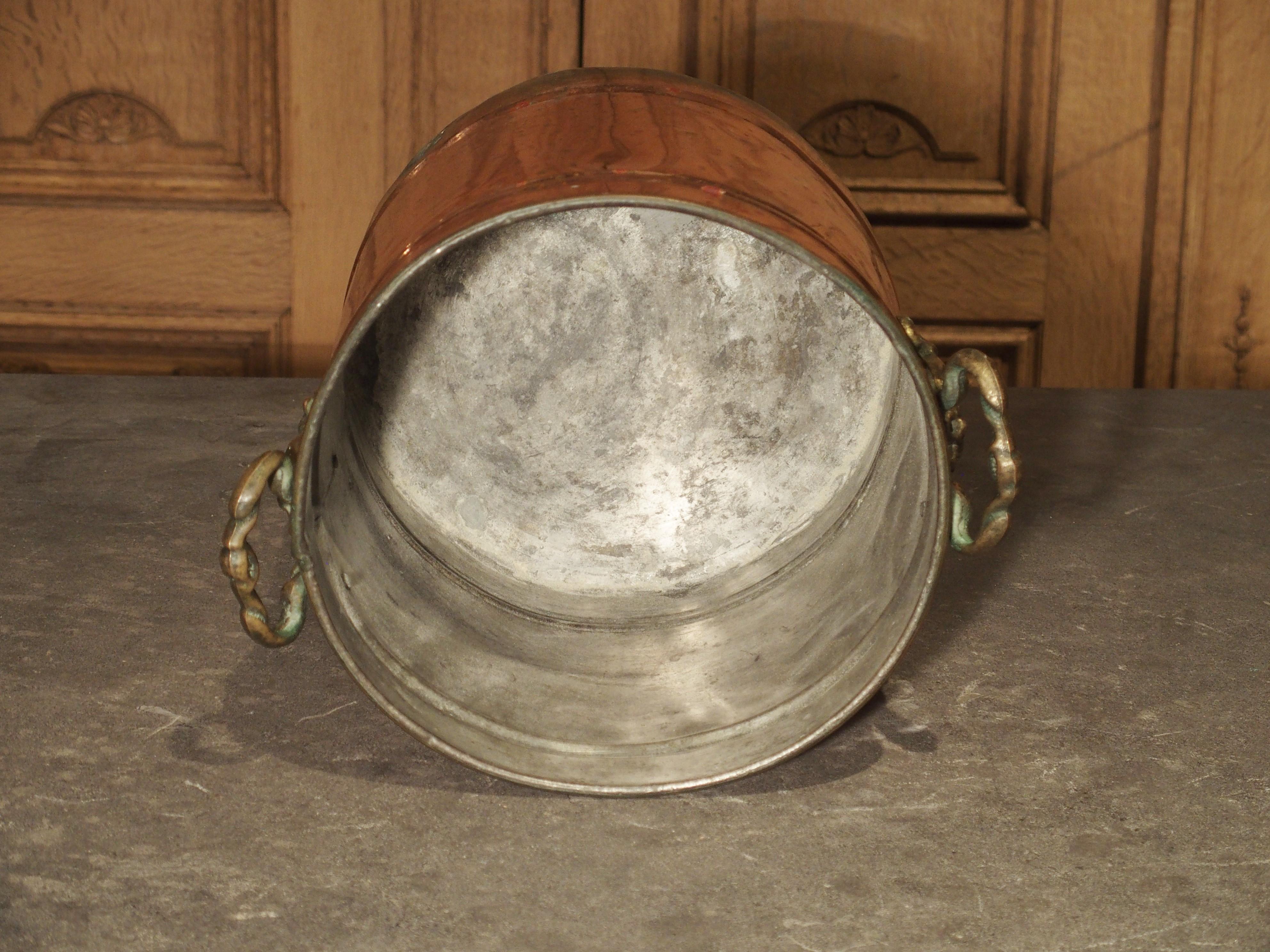 This English wine bucket is made of copper with decorative brass grape leaf handles on either side. It is perfectly round with three ribs of molding going around it. Perfect for your wine bottles, this English wine bucket will be a great addition to