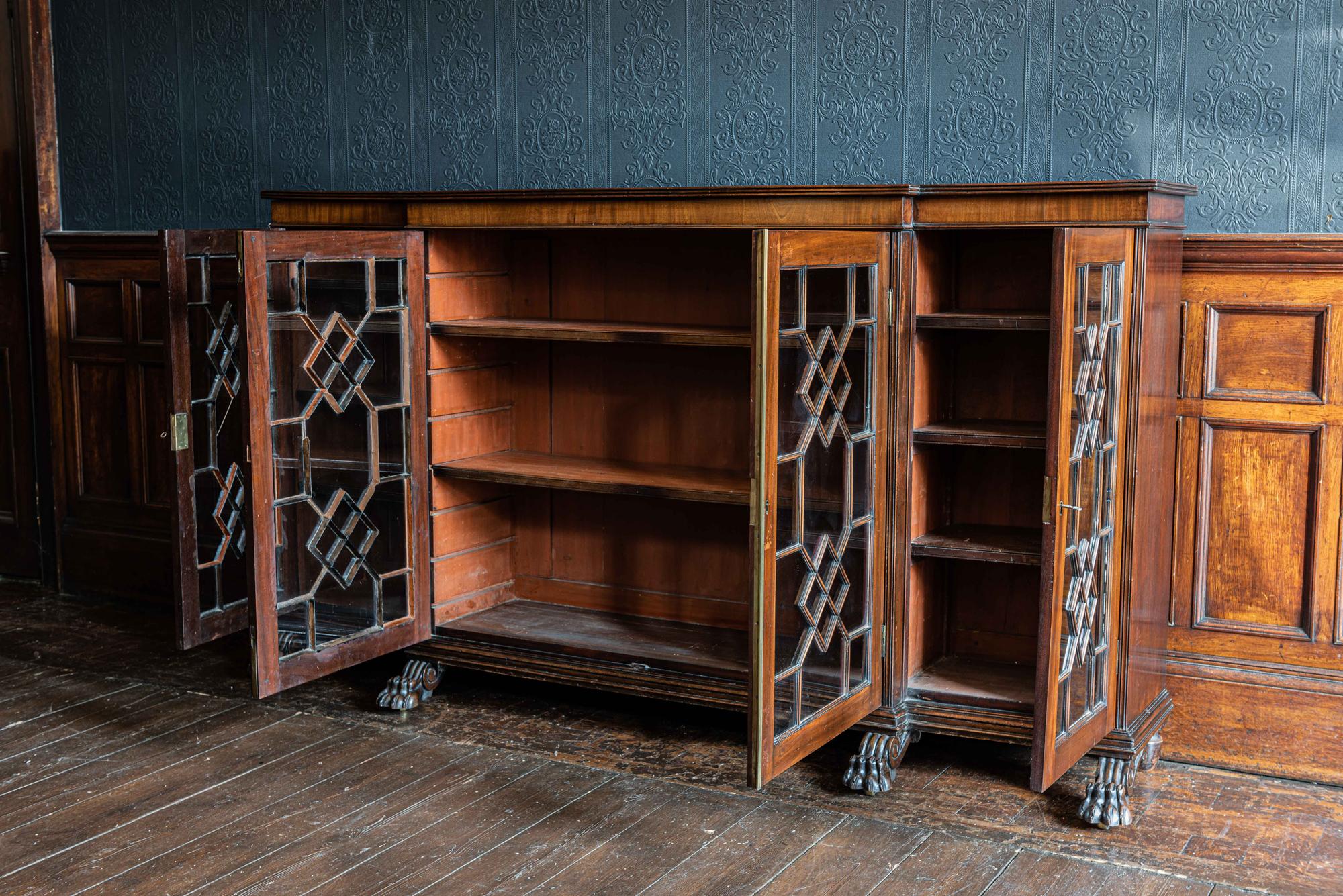 Country house mahogany breakfront bookcase,
circa 1895.

Carved mahogany lion paw feet with solid brass caster wheels under paws. Slim astragal glazing bars with brass central door closure strip and two working keys

Measures: W 209 x H 117 x D