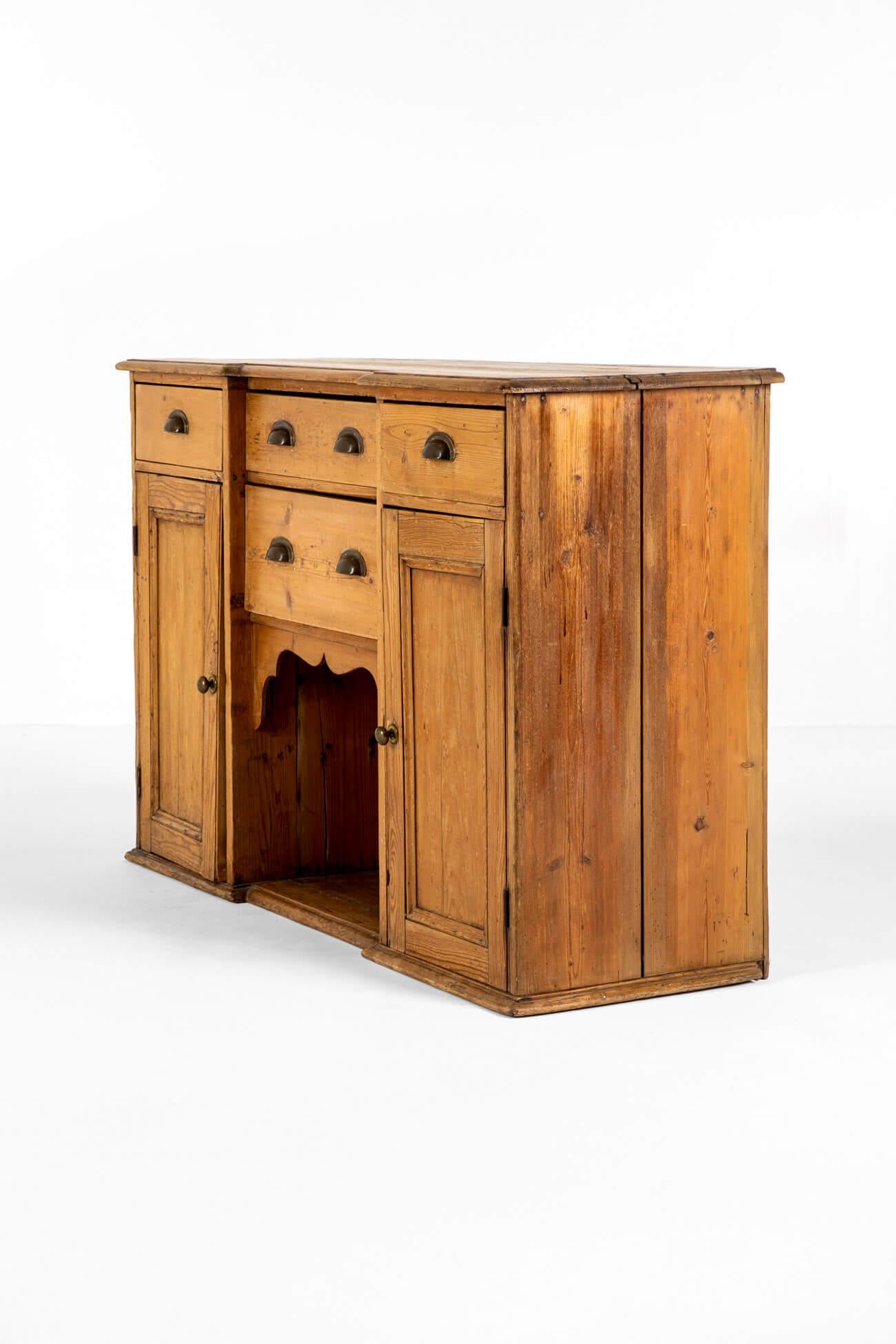 Un'affascinante base per comò in pino del XIX secolo con un generoso piano a due assi.

Con quattro cassetti e un'insolita nicchia centrale a forma di cane smerlato affiancata da armadietti con pomelli originali in ottone.

Questa base per comò,