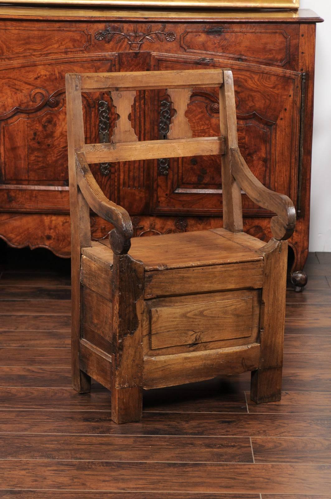 An English country pine chair from the early 19th century, with pierced back, scrolled arms and lift-top seat. This rustic country armchair features a simple pierced back, adorned with hourglass-shaped motifs. Two elegant scrolled arms connect the