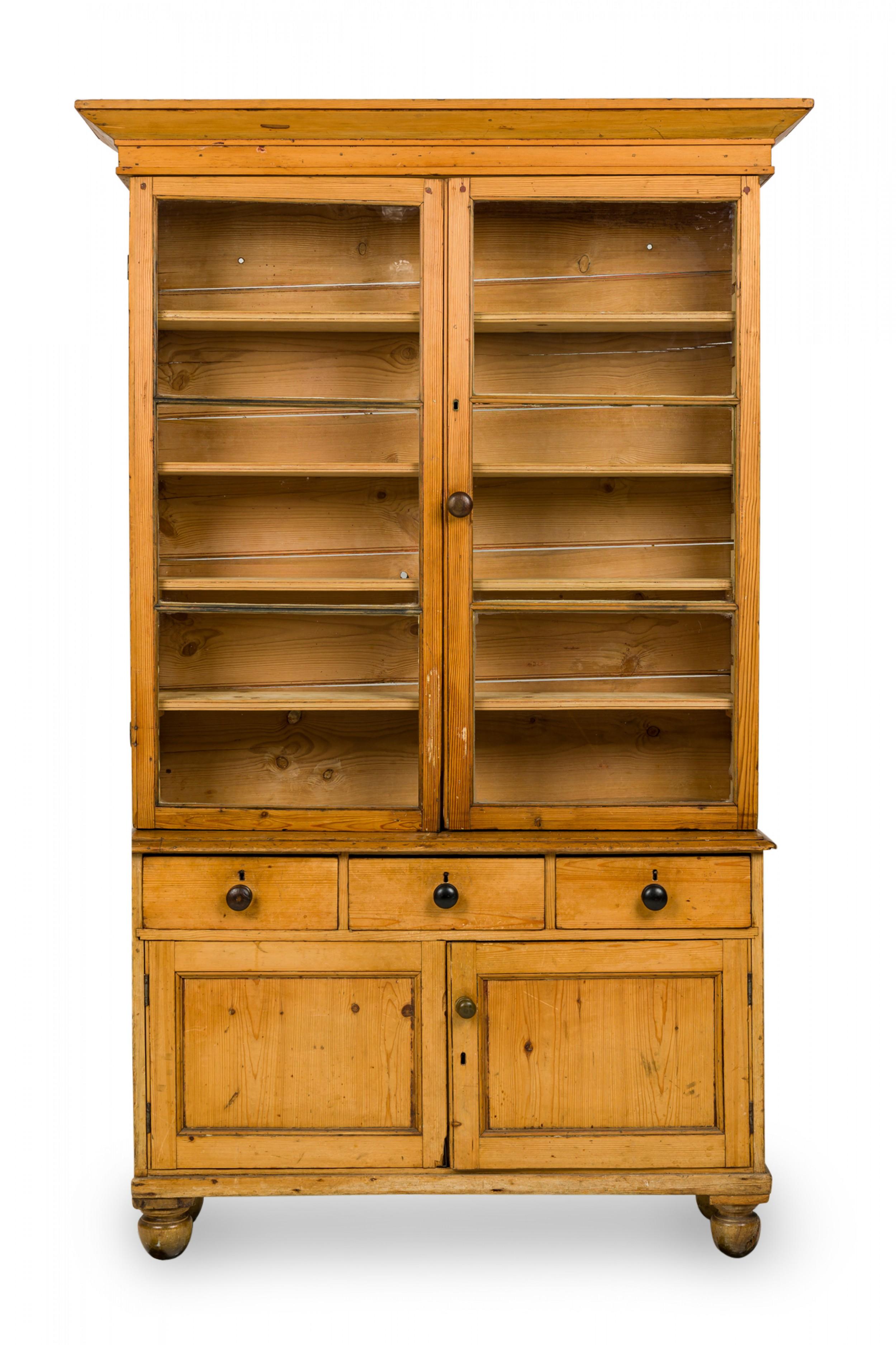 English Country-style hutch / cabinet with a pine wood case, pediment top, upper breakfront cabinet section with glass doors and four shelves above a lower enclosed base containing three drawers over a two door cabinet containing a dividing shelf,