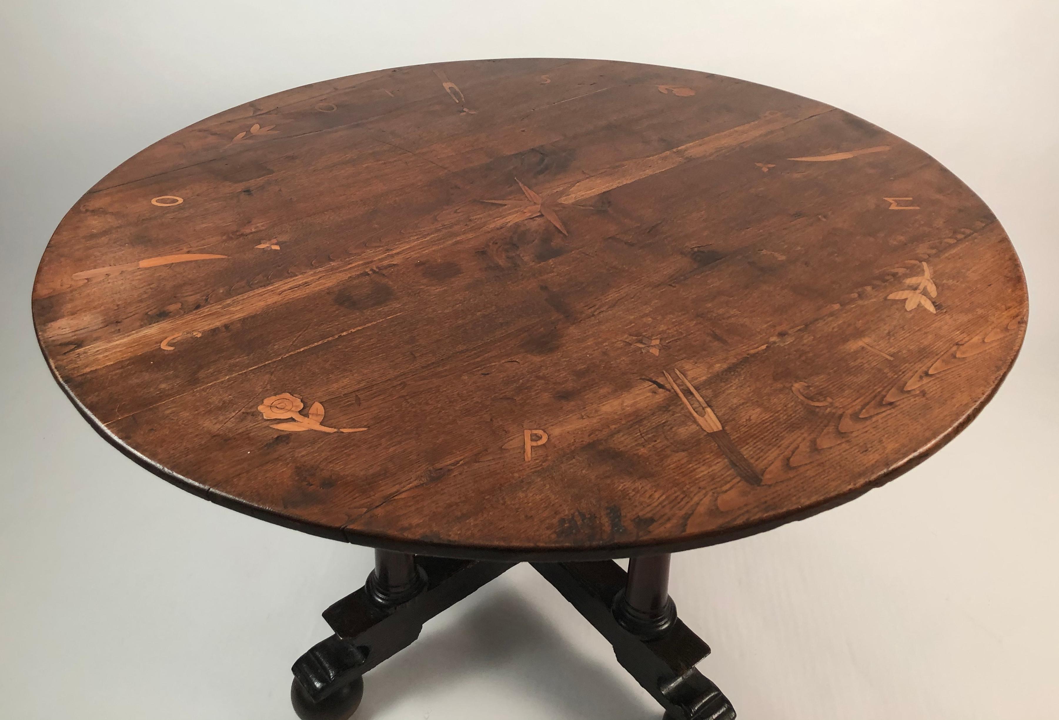 A charming and unusual circular breakfast or dining) table, with a 19th century English Country oak top inlaid with a fruitwood star in the center initials and forks and knives, representing place settings and the assigned seats, supported on a 19th