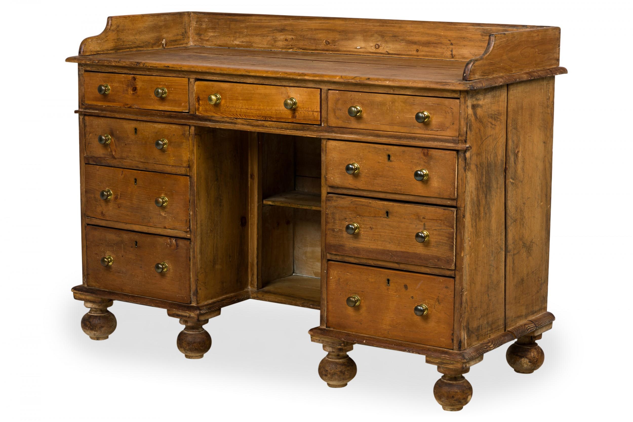 English Country (late 19th Century) pine wood kneehole desk having a scalloped gallery, three drawers in the frieze on the front side, a bank of three drawers below with brass pull handles, a central shelved open compartment vanity panel, standing