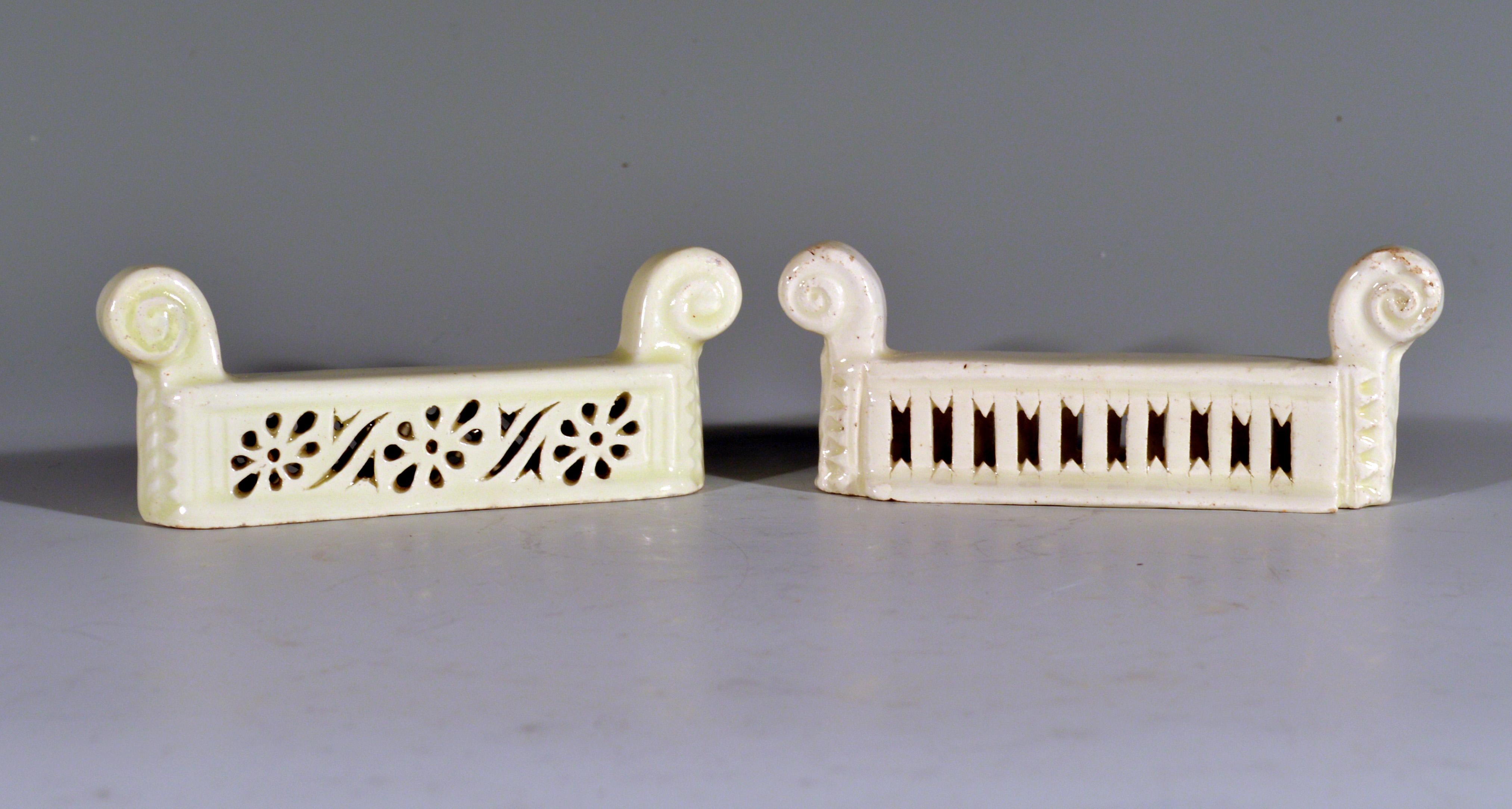 Creamware knife rests,
Italian,
Circa 1810-1820
   
The two rests are of similar form with a raised scroll terminal to each end. One with pierced stylized flower heads and leaves in the central panel to each side and the second with a column design