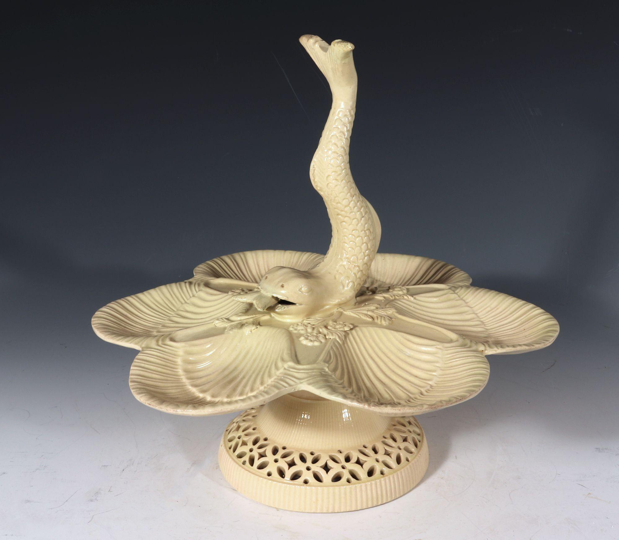 English creamware sweetmeat centerpiece stand with Dolphin,
Attributed to Leeds, Yorkshire
circa 1775-1790

The plain creamware sweetmeat centerpiece stand has six conjoined moulded scallop shell shaped trays, each tray with two overlapping