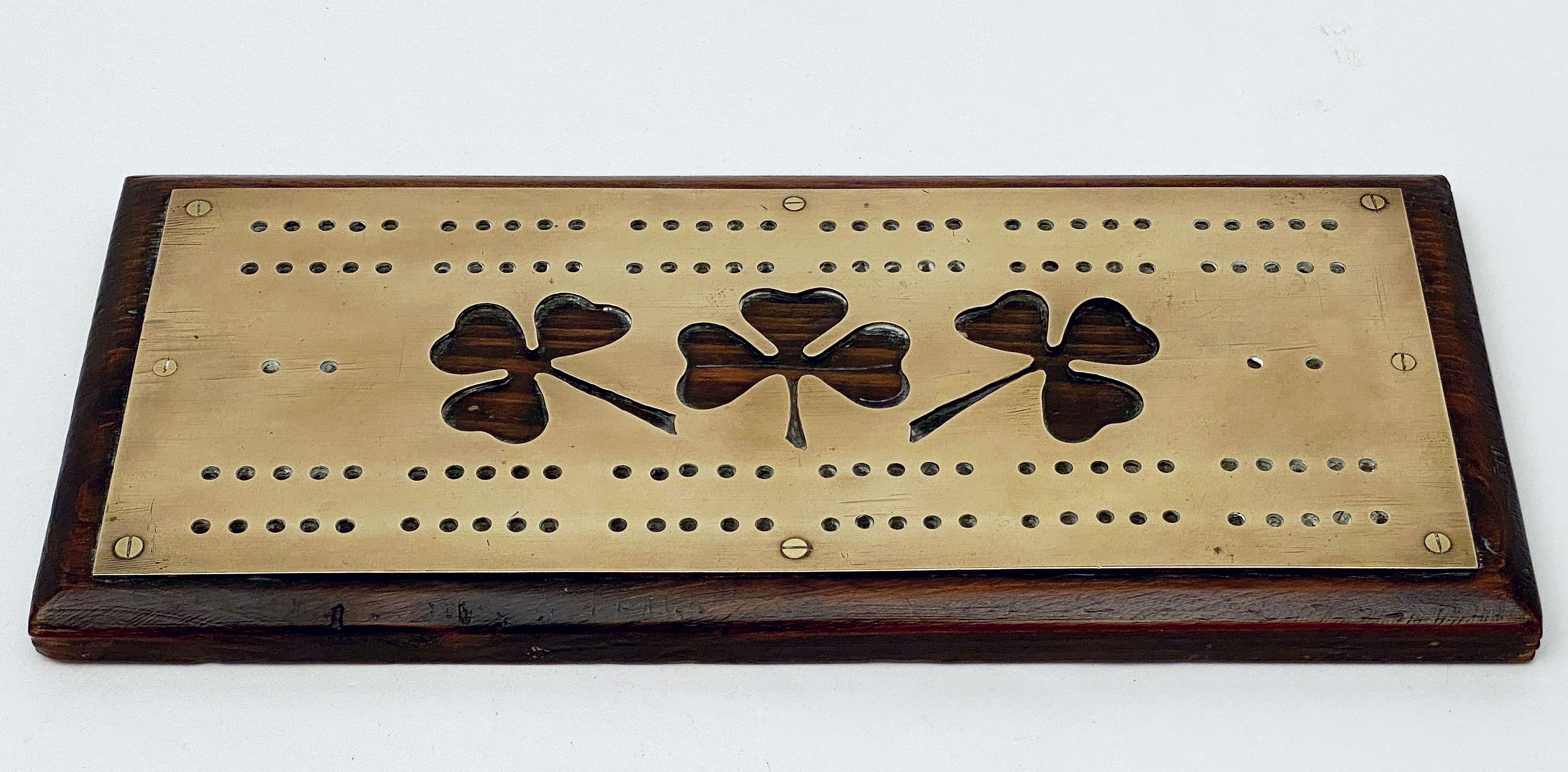 A fine English rectangular cribbage or games board featuring a brass top with a design of three shamrocks and pierced holes for game pegs, mounted to a moulded wood base.