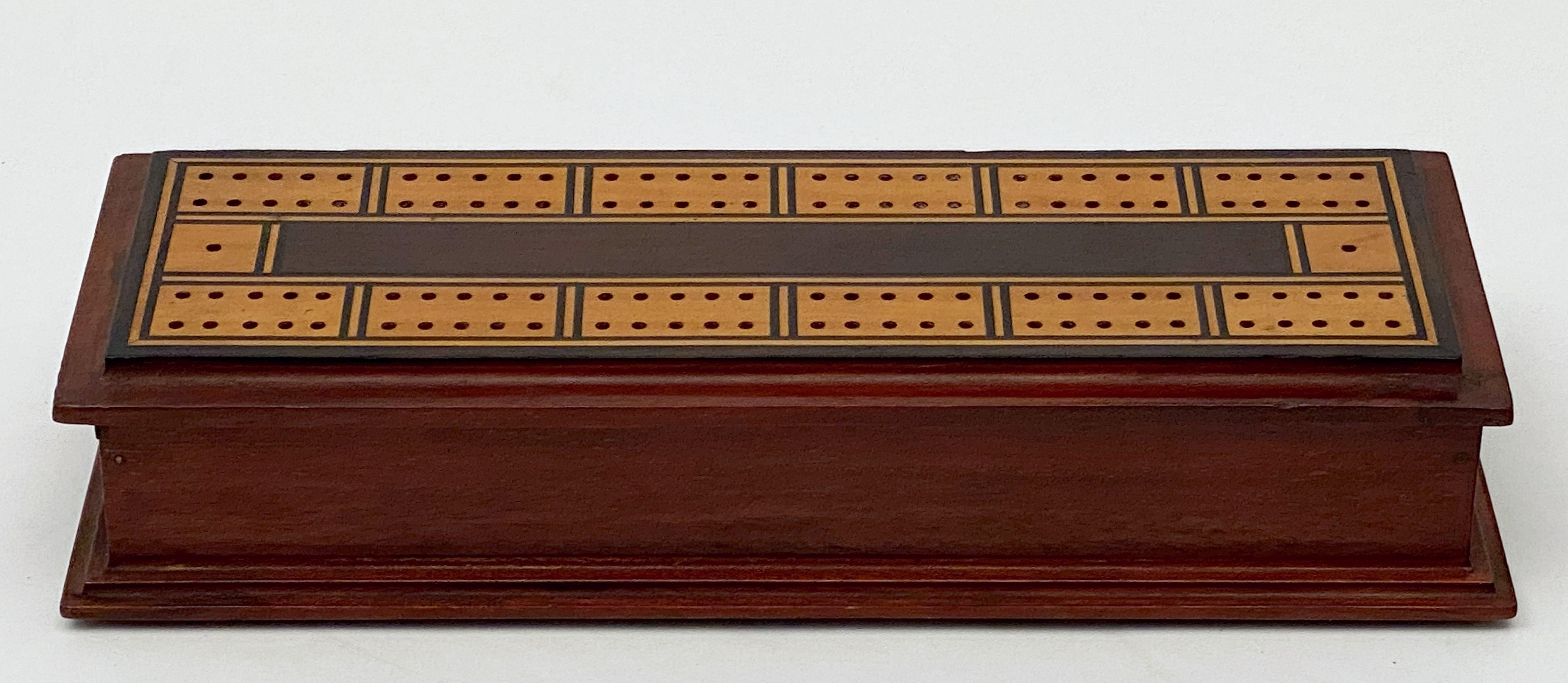 A fine English rectangular cribbage board or game box from the 19th century featuring a handsome contrasting inlay on the removable lid - the body of the box in mahogany, opening to a compartmentalized interior with four bone pegs. The underside of