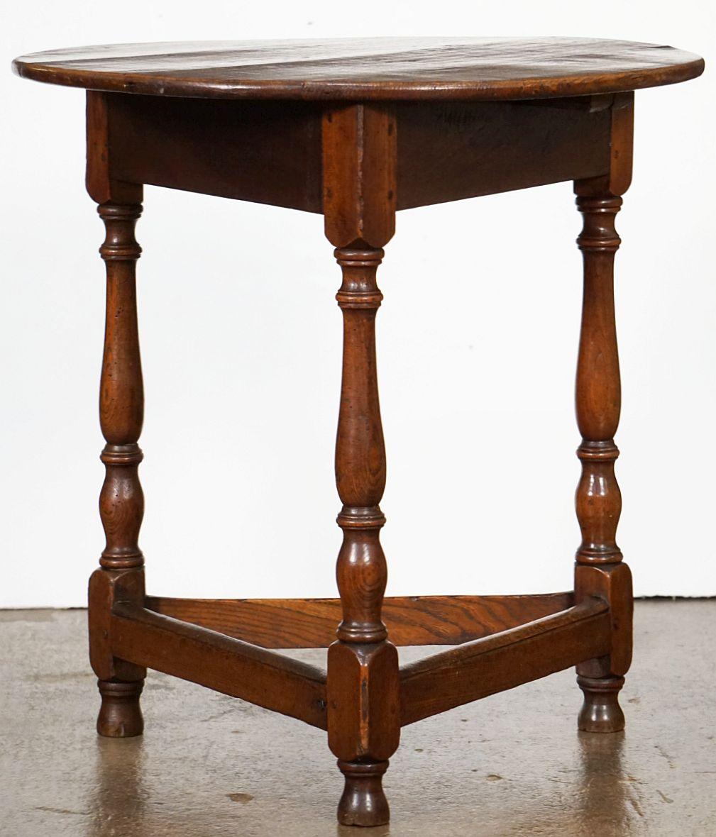 A fine English cricket table of patinated oak and ash from the late George III period, featuring the traditional round or circular top over a tripod base with turned supports, pegged joins, and triangular under-tier foot brace.

Makes a nice