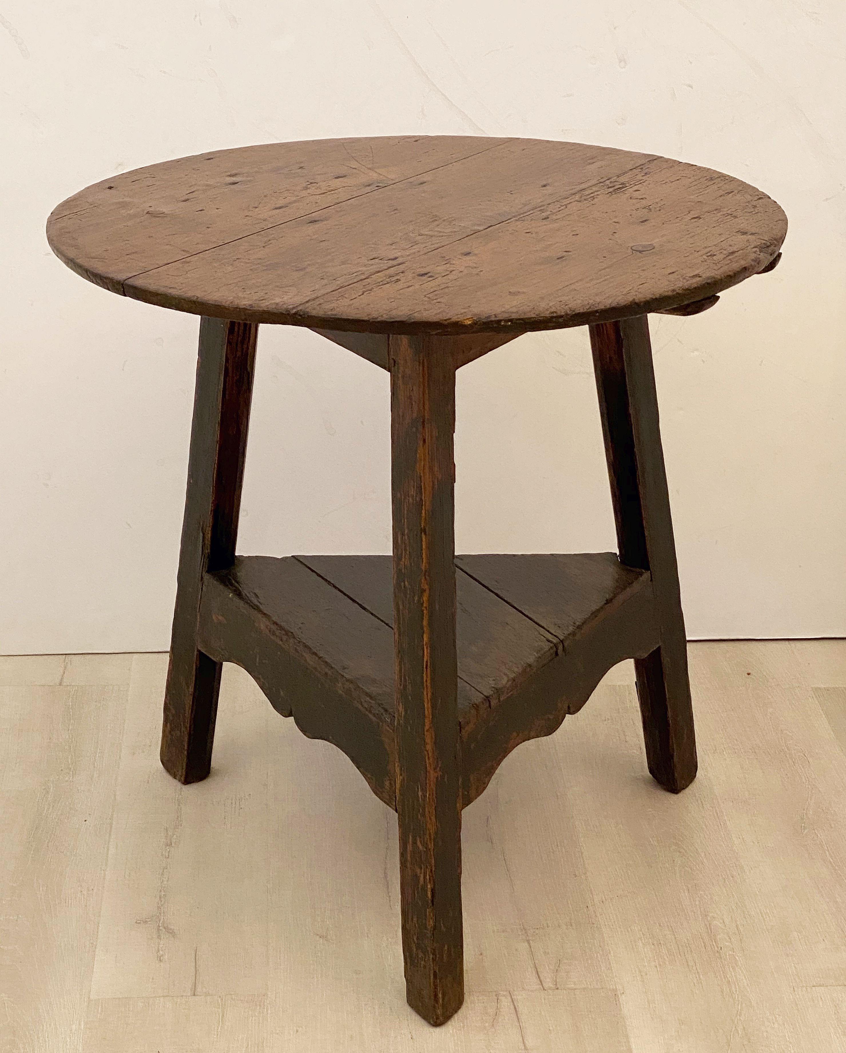 A fine English cricket table of aged pine featuring the traditional round or circular top over a tripod base of painted pine with triangular under-tier shelf.
The under-tier shelf with decorative ogee accents.

Makes a nice occasional table or