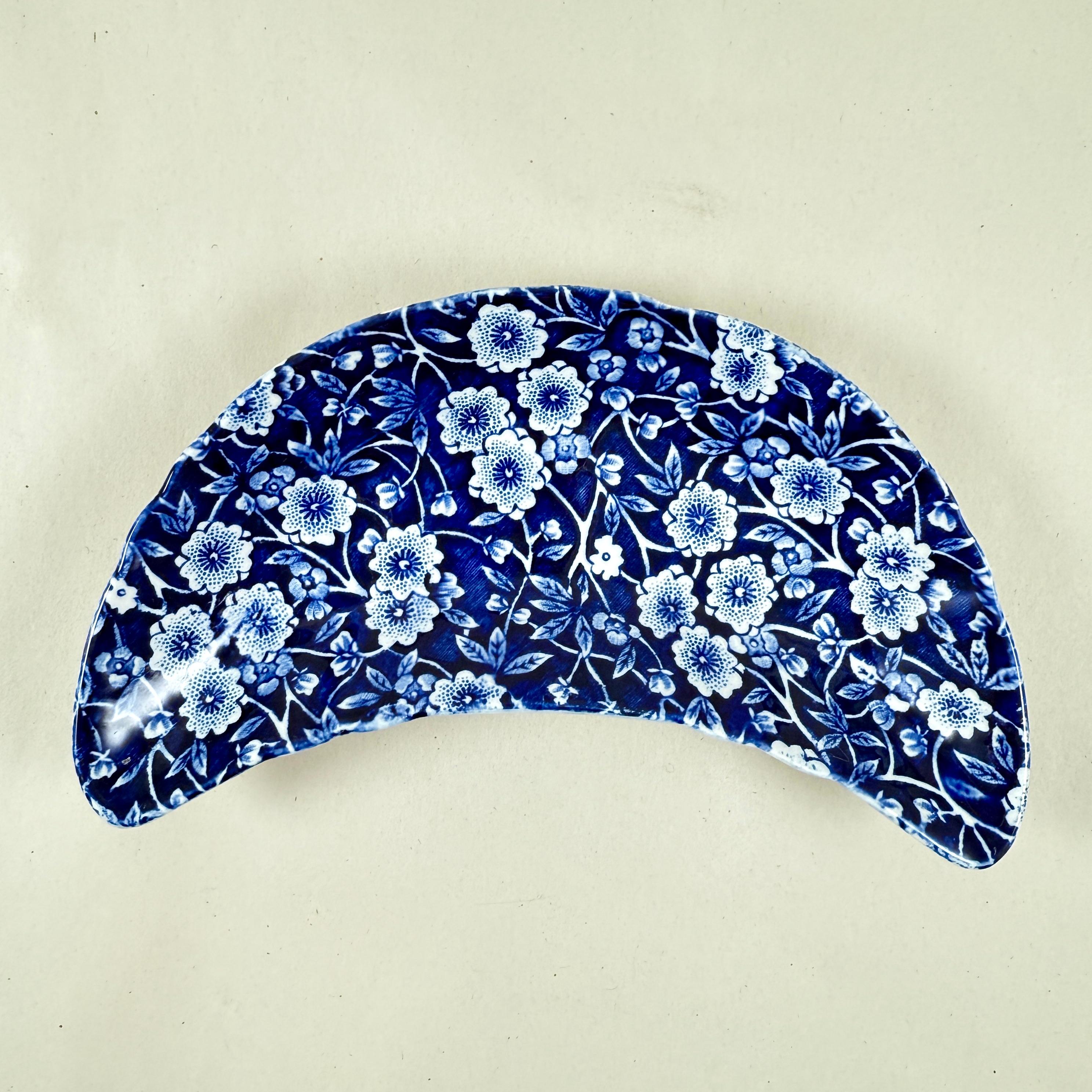 A crescent shaped bone dish in the Blue Calico pattern by Crownford China, Staffordshire, England, circa 1960s.

This pattern was first made by Burleigh Pottery in 1851. It is inspired by 19th-century indigo fabrics and features rich cobalt blue