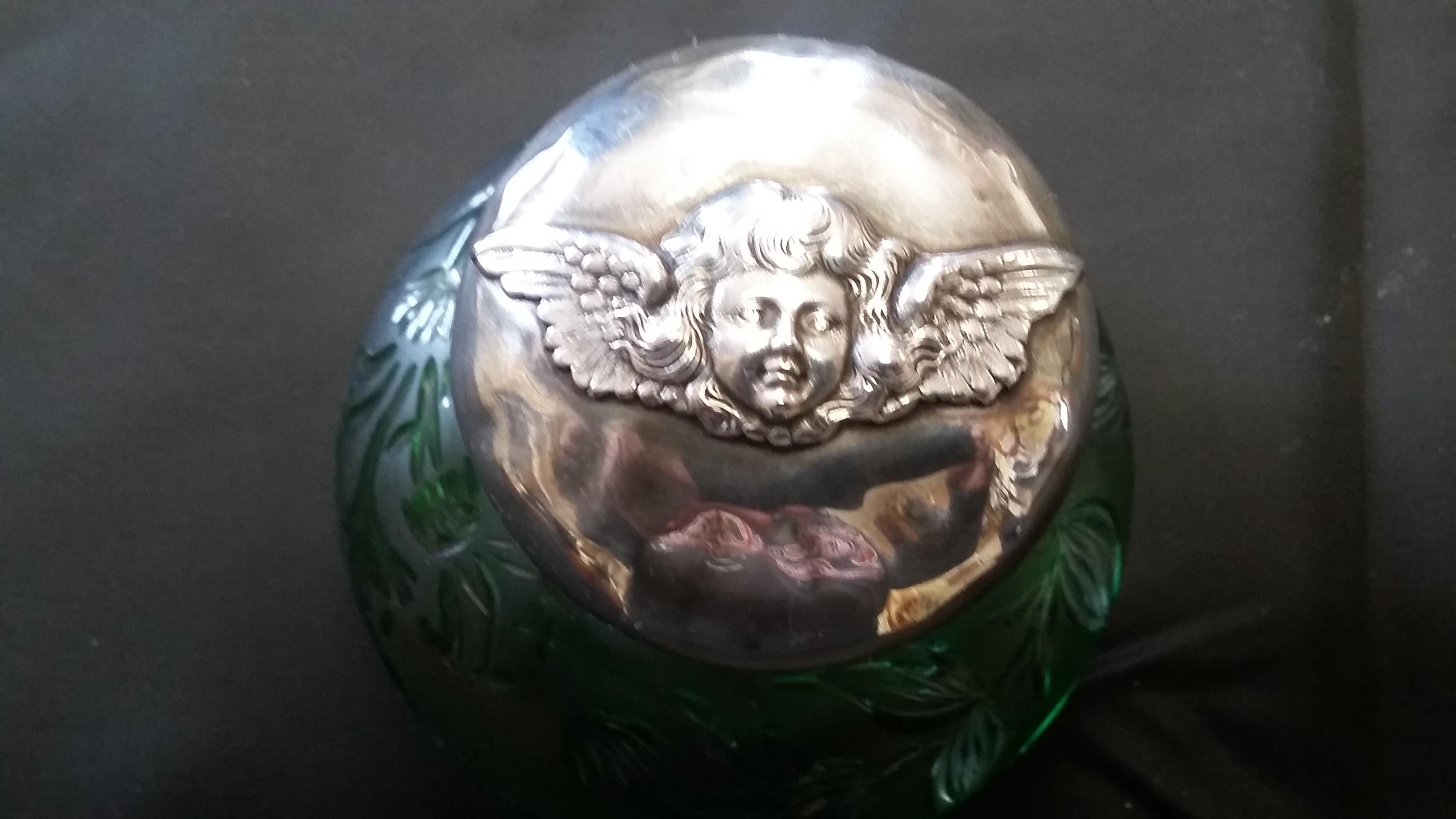 Beautiful green crystal inkwell from England circa 1890. This inkwell is complete with a glass insert and a sterling silver lid with an unique angel (cherub) motif on the lid. Lots of design on the inkwell with cut glass details on the bottom. 
On