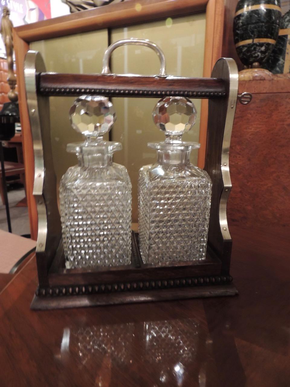 A 1920s Tantalus with crystal decanters, a rich wooden case trimmed in nickel with lock and key. Highly faceted bottle stoppers beautifully reflect the light. This is a perfect piece for display or serving. It was made for the importer Rodolfo