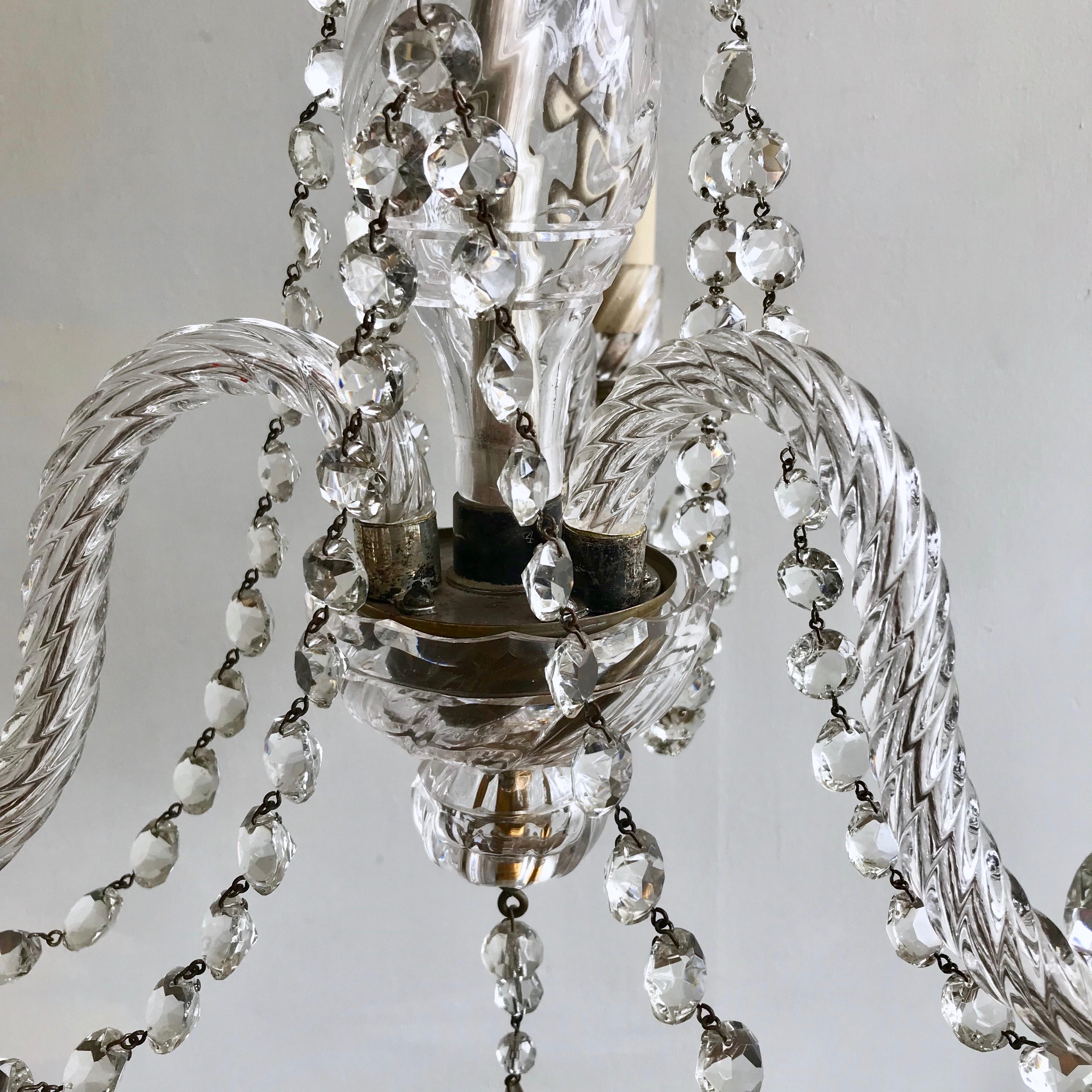 An English cut crystal chandelier originally a candelabra which has been electrified dates from the late 1800s. The chandelier has three arms each with an SES lamp holder. Each arm is connected with crystal swags which also connects to the upper
