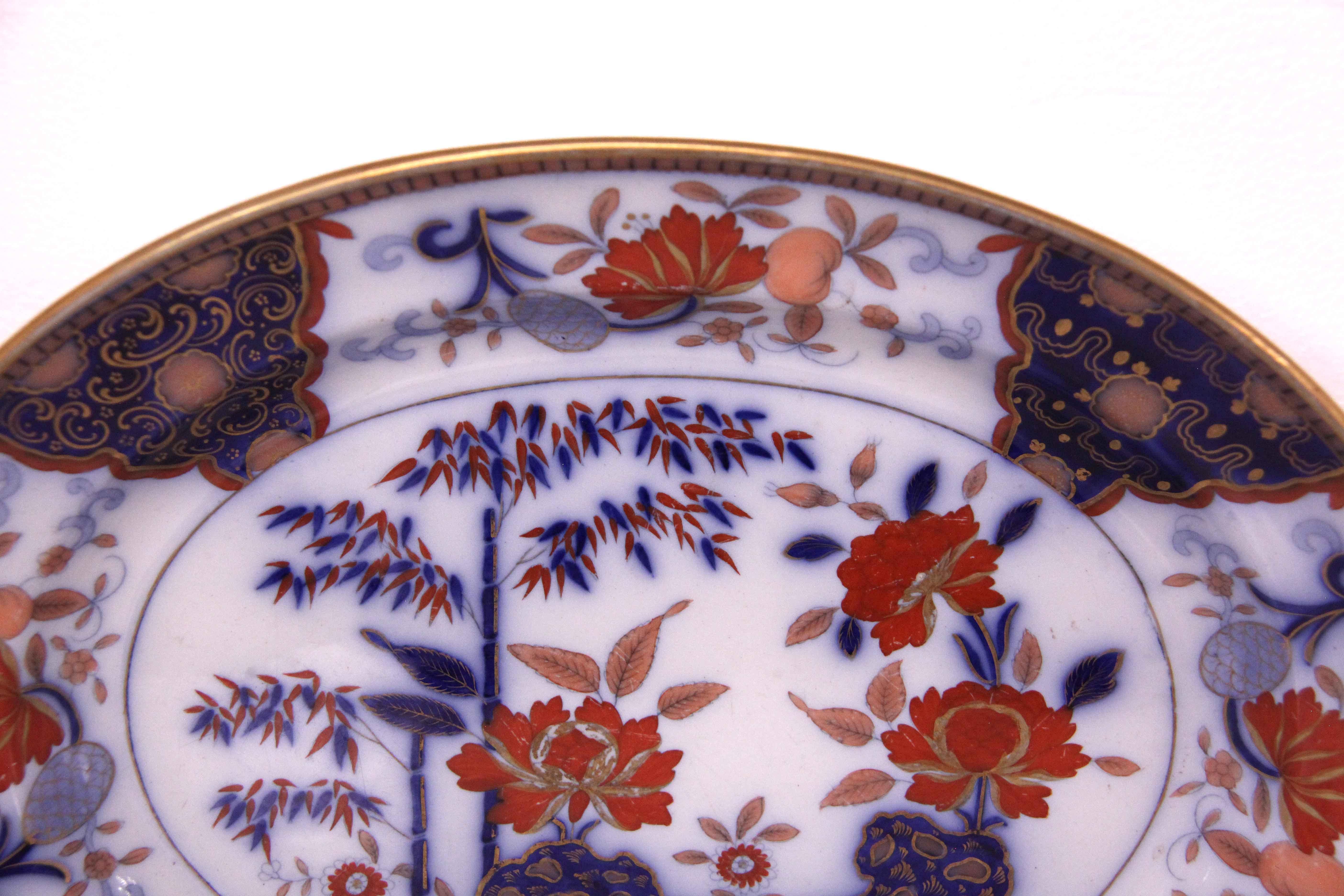 English Davenport flow blue ironstone platter, with a gilded rim, the border is decorated with stylized flowers and foliate, the interior of the platter has similar stylized flowers, foliate and bamboo stalks. There is gilding throughout the piece