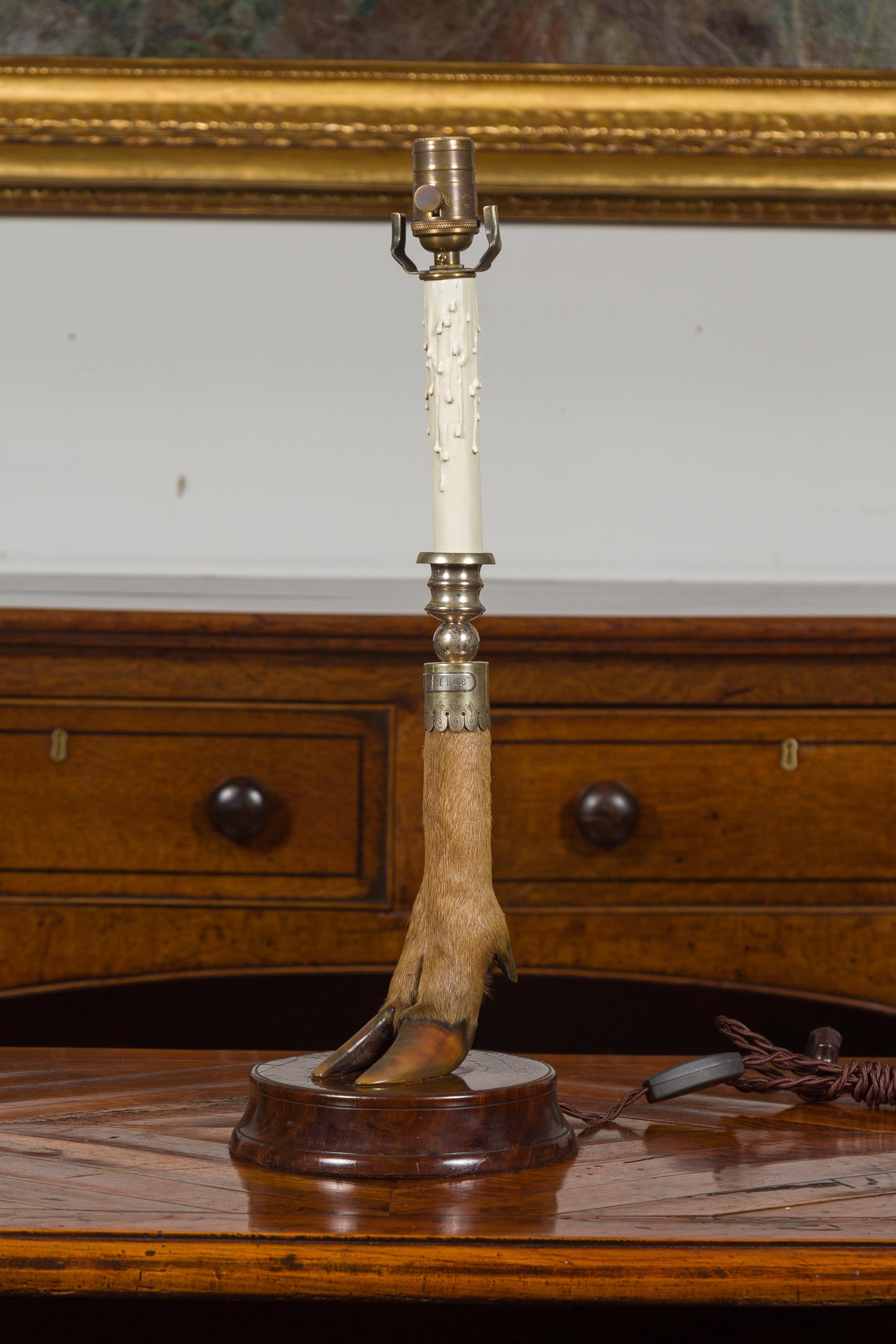 An English deer leg table lamp from the early 20th century, mounted on a circular wooden base. Created in England and dated 1908 on the label, this table lamp draws our attention with its slender deer leg mounted on a circular wooden base. Wired for