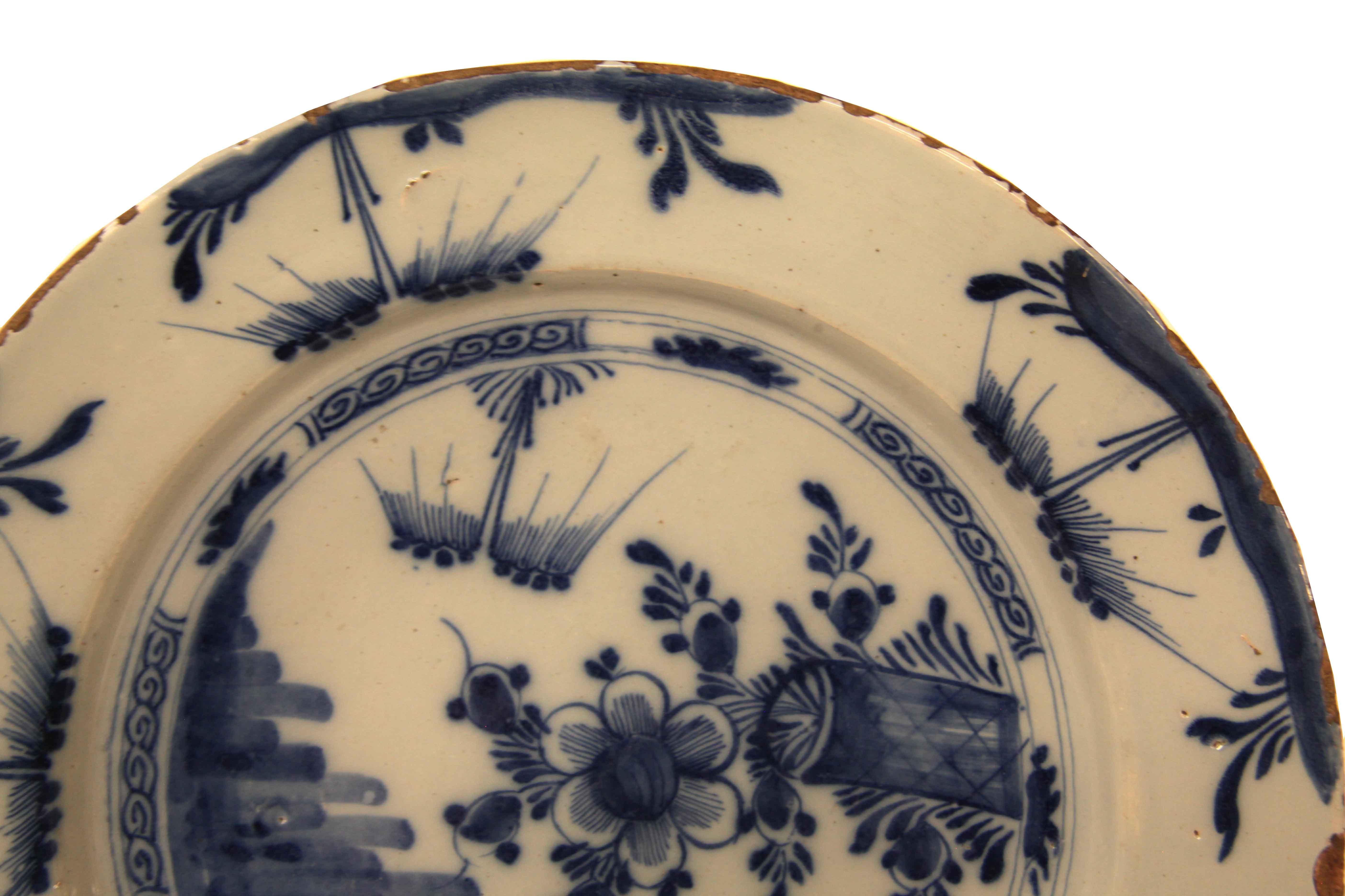 English Delft blue and white charger, the border with repeating foliate decoration, center with stylized flowers and foliate; on the back there is a blue mark in the center; the loss of glaze around the perimeter of the rim is consistent with the