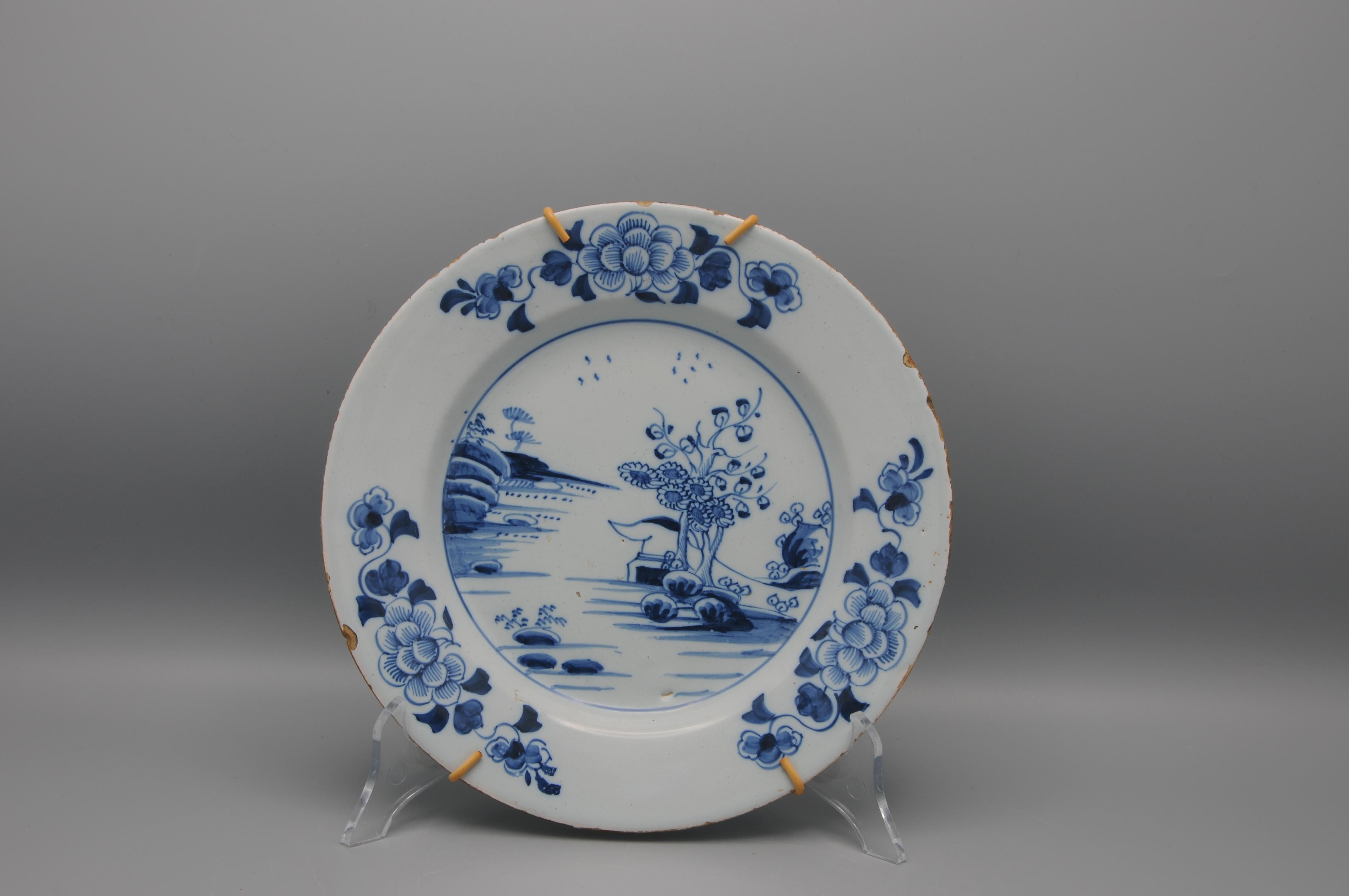 A beautiful English Delftware plate, hand-painted in rich cobalt blue, featuring a Chinoiserie-inspired landscape with a floral border. I cannot help thinking that I am seeing the tail of a deer or other animal hiding behind the rocks, which is one