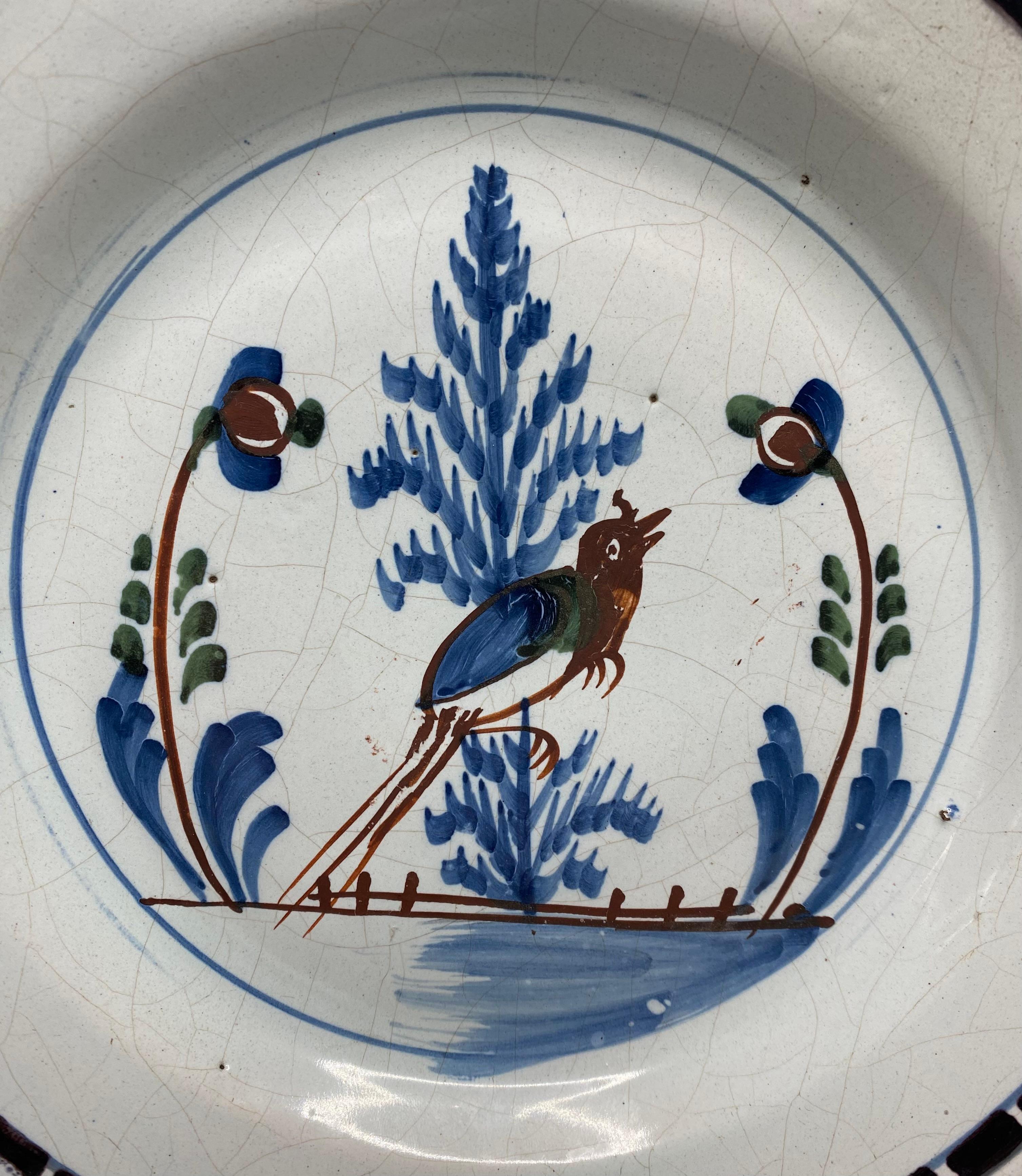 Rare English delft pancake plate, London c. 1750. Naively hand painted to the centre, in polychrome enamels of underglaze blue, manganese, green and iron red, with an amusingly oversized long tailed bird perched amongst foliage, above a fence. The