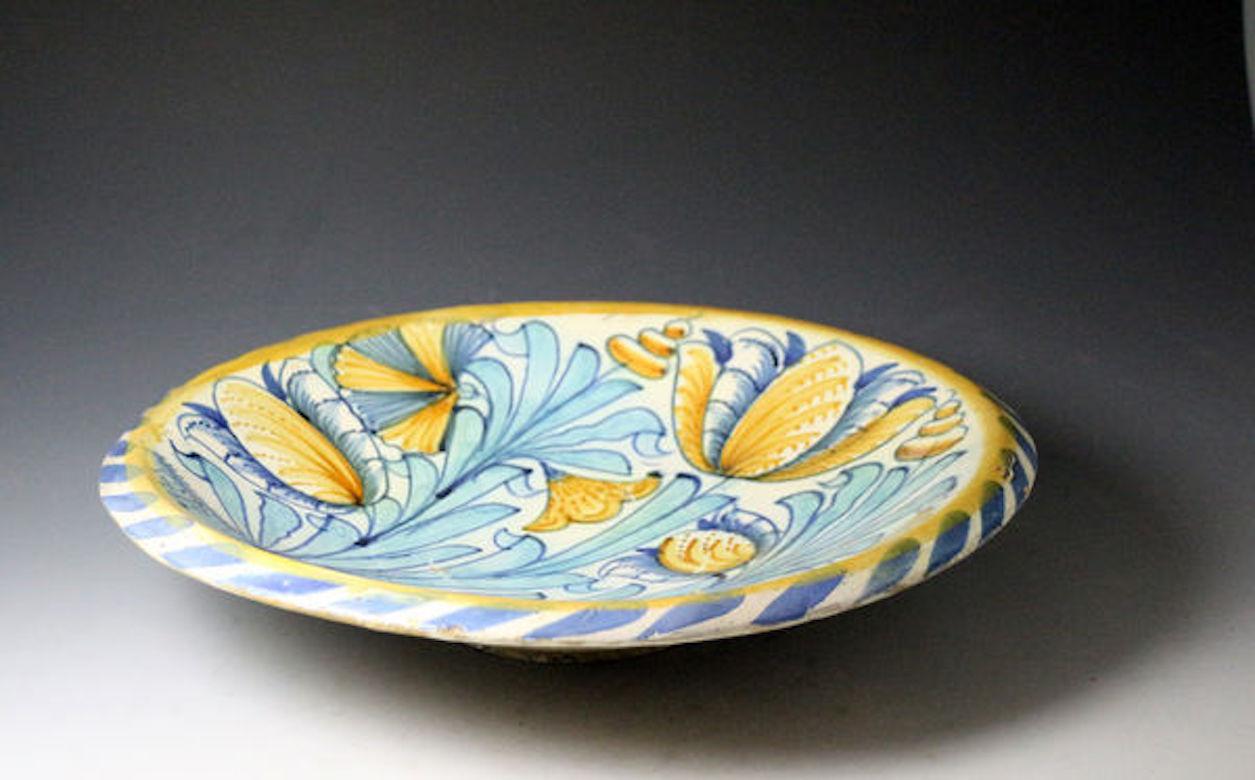 Dated: circa 1680, London, England

English pottery delftware charger with a blue dash and yellow line border and a lead glaze back. The centre is boldly decorated with tulips, carnations and buds with leaves growing from a low mound. The color