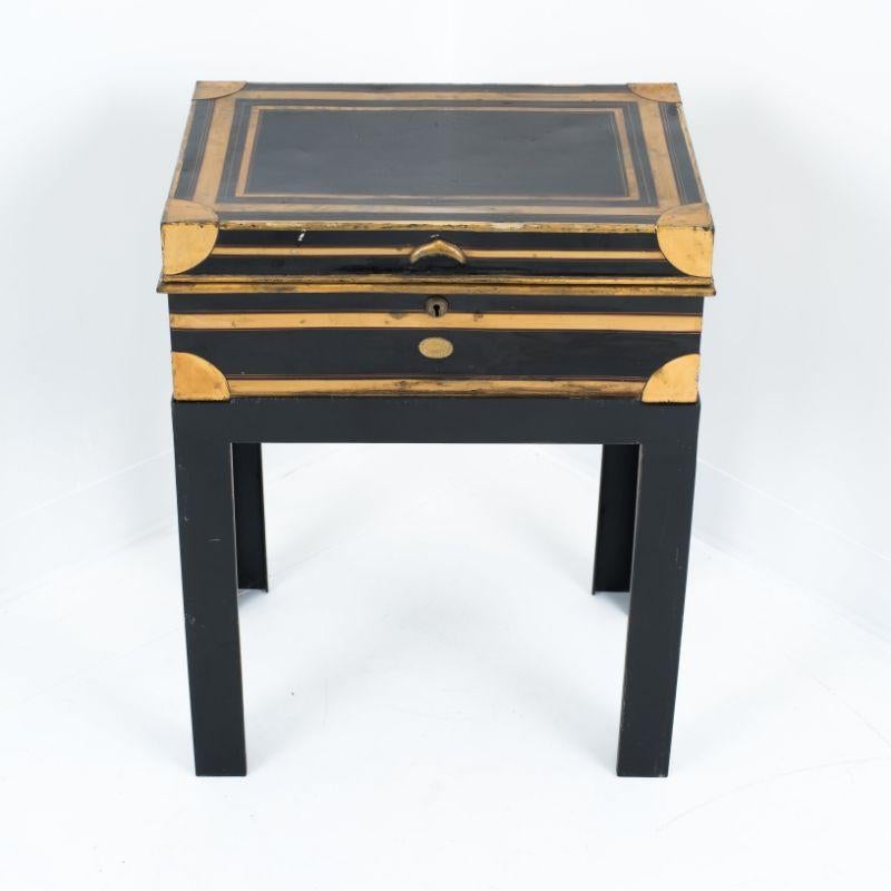 Black painted and gilt banded steel dispatch box with interior fitted for writing. The case has a lock, brass reinforced corners, and the sides are mounted with cast brass bail handles. The interior is painted celadon green and is mounted with a