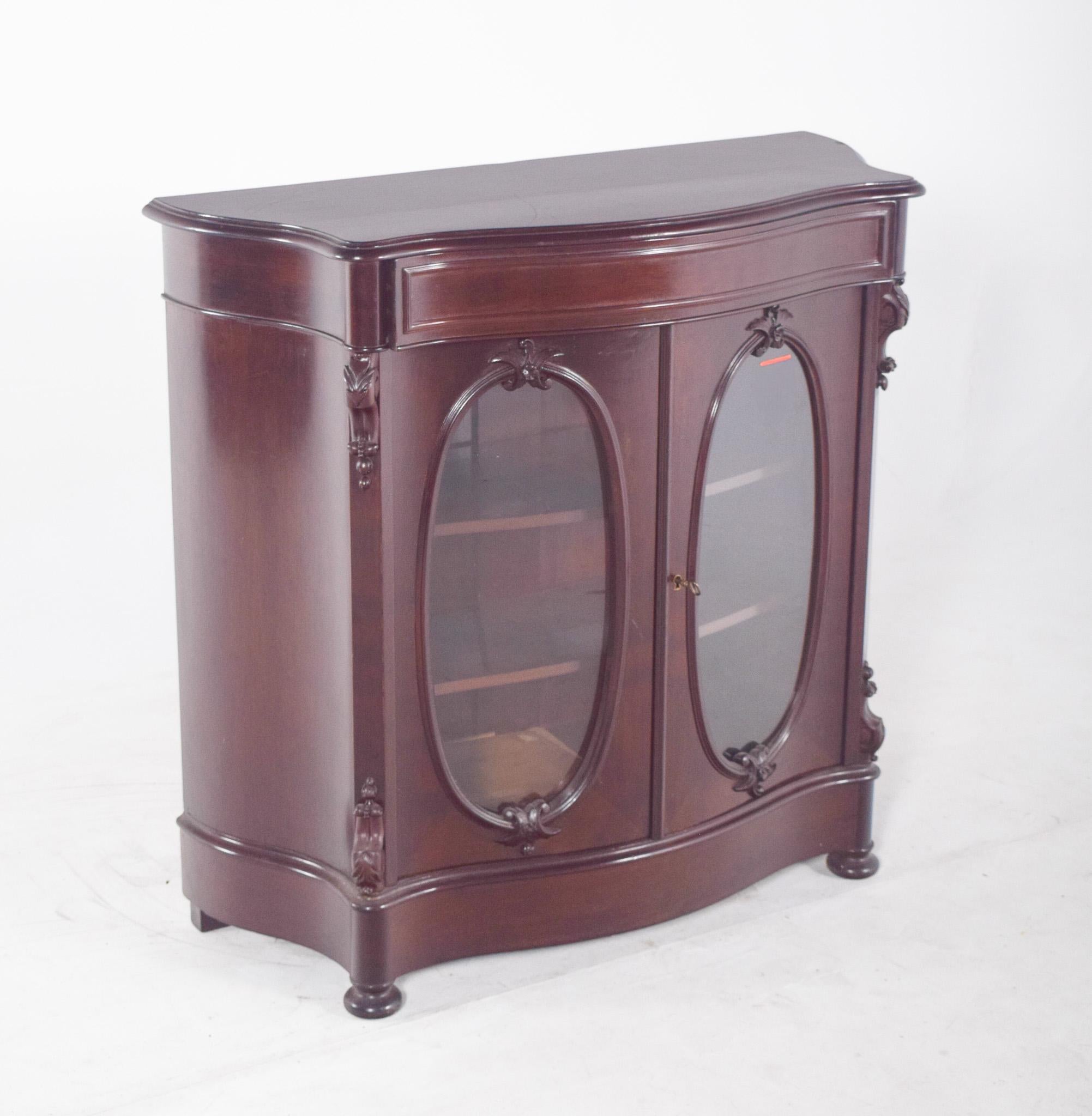 Doppeltürige Vitrine. Mit einer leicht gewölbten Front und zwei ovalen, verglasten Türen, die mit von Pflanzen inspirierten Skulpturen verziert sind. Die seitlichen Säulen, die mit dem Hauptteil verbunden sind, weisen kleine Kapitelle und