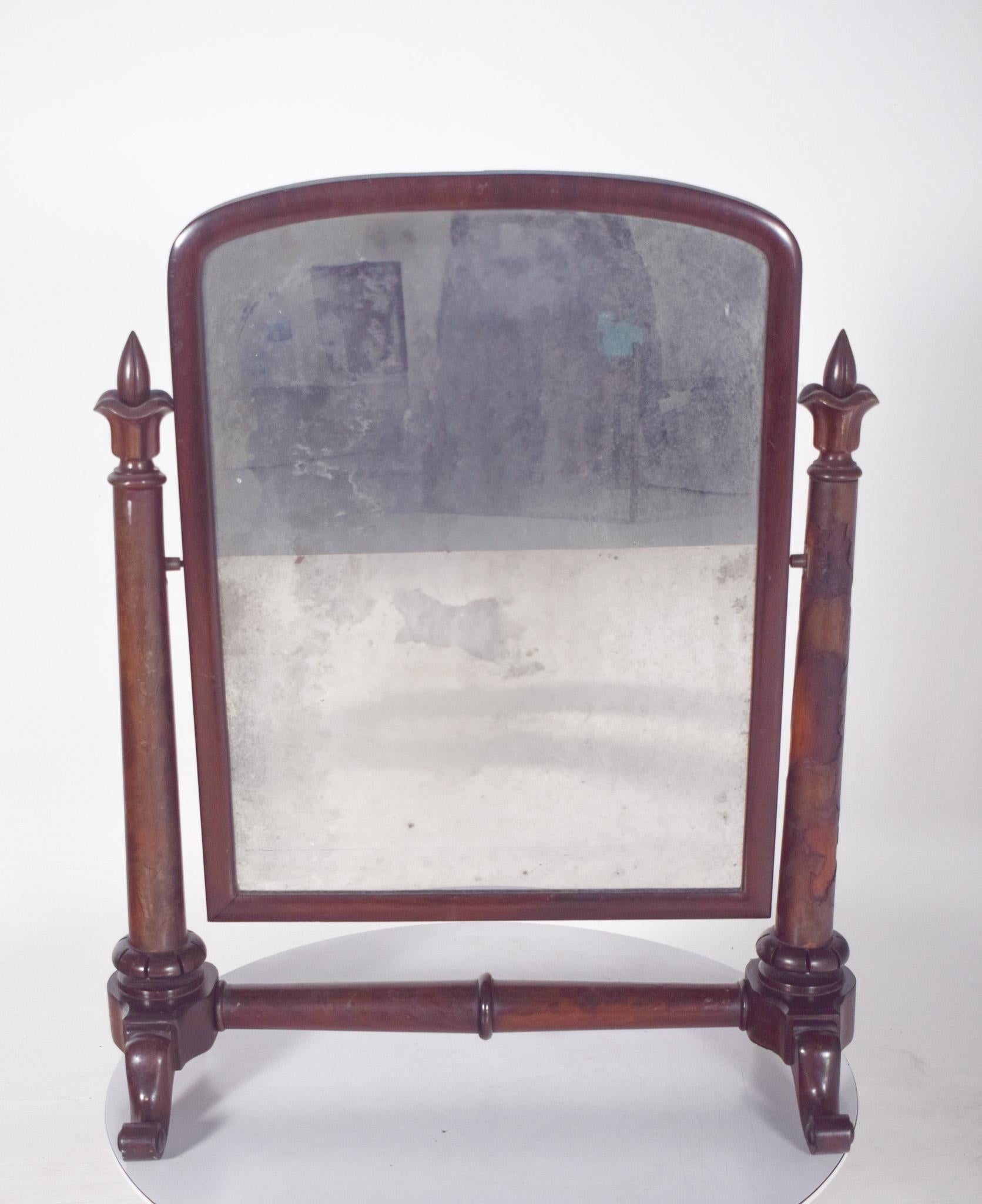 Specchio da toilette con bordi torniti. Lo specchio è rettangolare, con gli angoli superiori arrotondati ed è inserito in una cornice semplice ed elegante, sostenuta da due colonne tornite con dettagli floreali nella parte superiore, a forma di