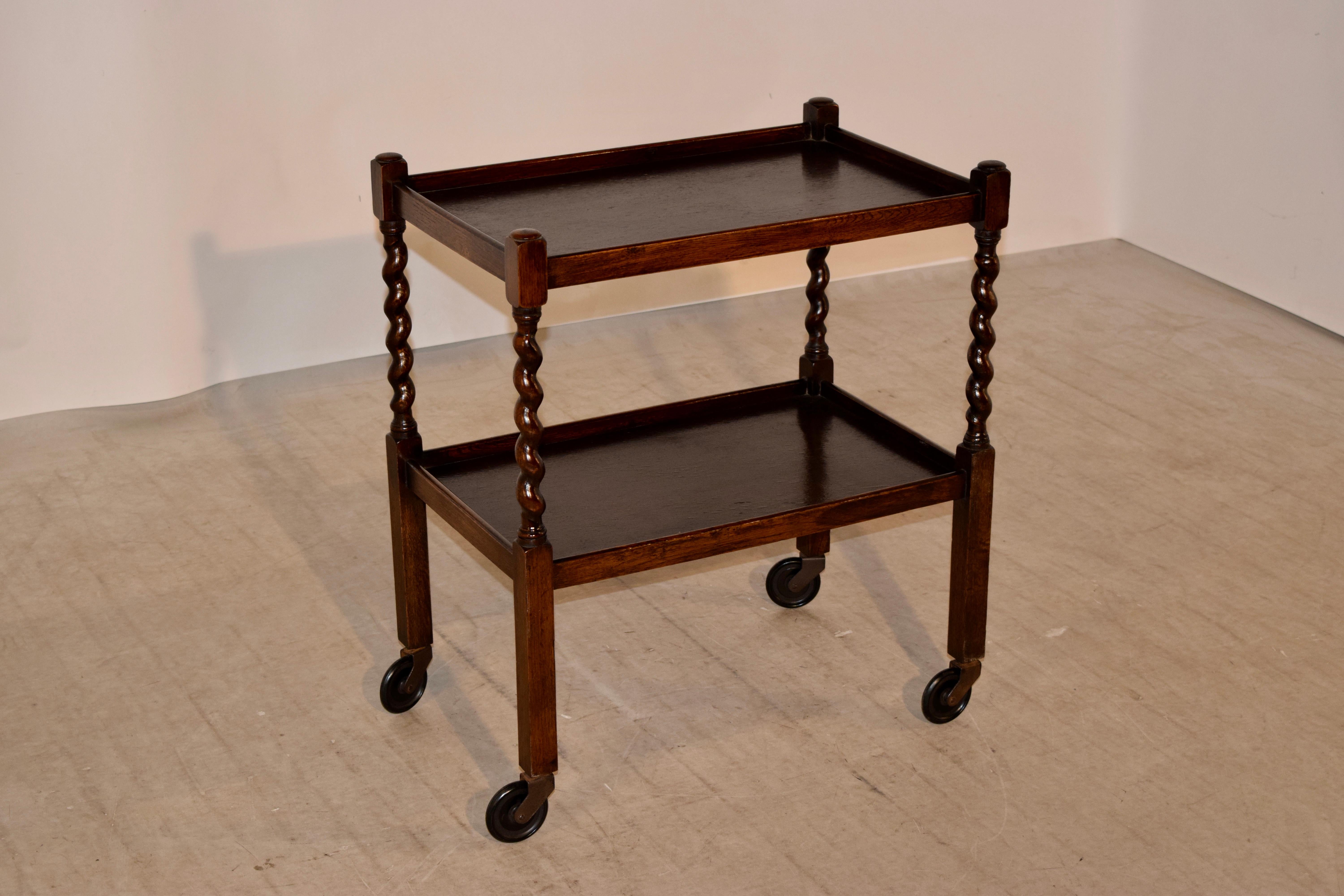 Edwardian drinks cart from England made from oak. The cart has two shelves, both with galleries around the edges and supported on hand-turned barley twist and simple legs, raised on original casters.