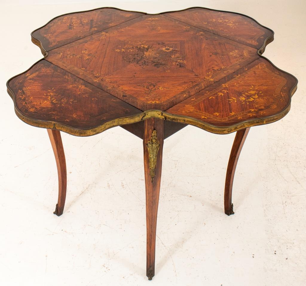 English drop leaf games table with four leaves, top with inlaid wood floral motif, parcel gilt metal decoration to cabriole legs. Measures: 29.5