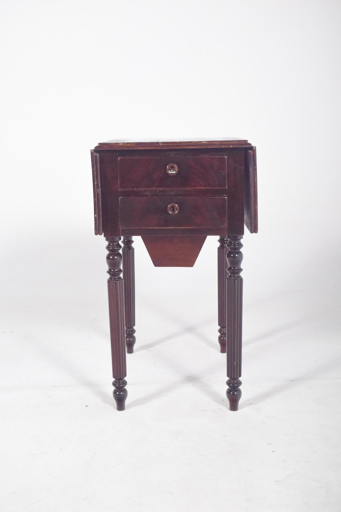 Rectangular flap table. The flaps are supported by hinged brackets that extend from the lower structure when open. The base has four turned legs with vertical grooves and carved details at the ends, typical of the neoclassical or Empire style. It