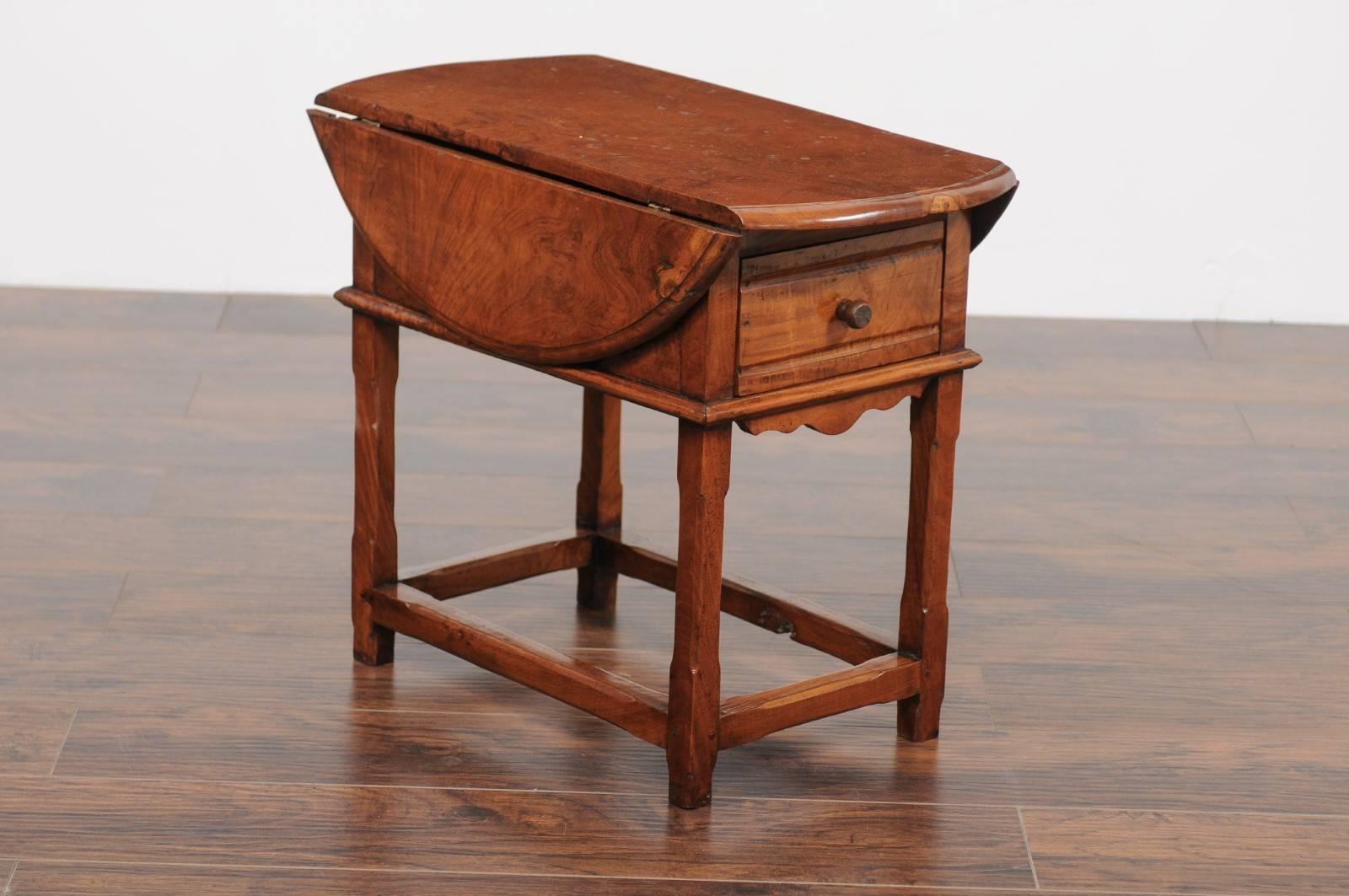 An English yew wood drop-leaf side table from the second half of the 19th century, with circular top, single drawer and side stretcher. This English yew wood table features a top made of two drop-leaves and rounded edges, sitting above a simple