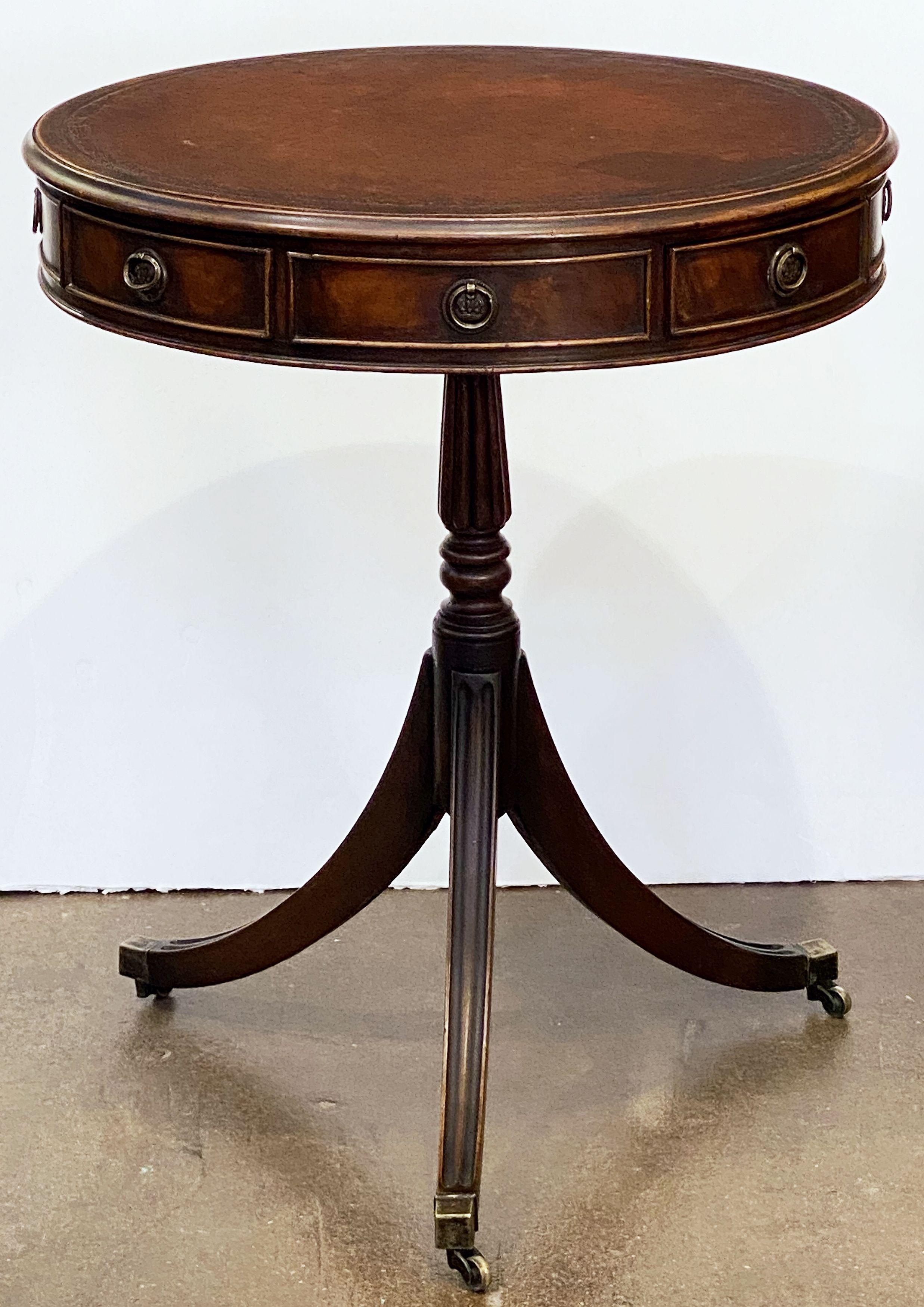 A fine English drum table of mahogany from the Edwardian era, retaining its original leather top above a frieze fitted with four beaded drawers and four faux drawers, each drawer with brass hardware, with a turned stem below raised on three sweeping