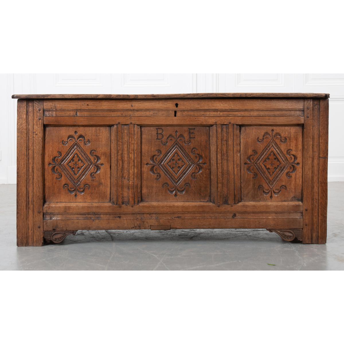 A gorgeous oak coffer or trunk from the 1700s, England. The front façade has three panels that have been meticulously carved into identical patterns with additional carvings at the base. The center panel has the initials ‘B.E.’ carved into the top,