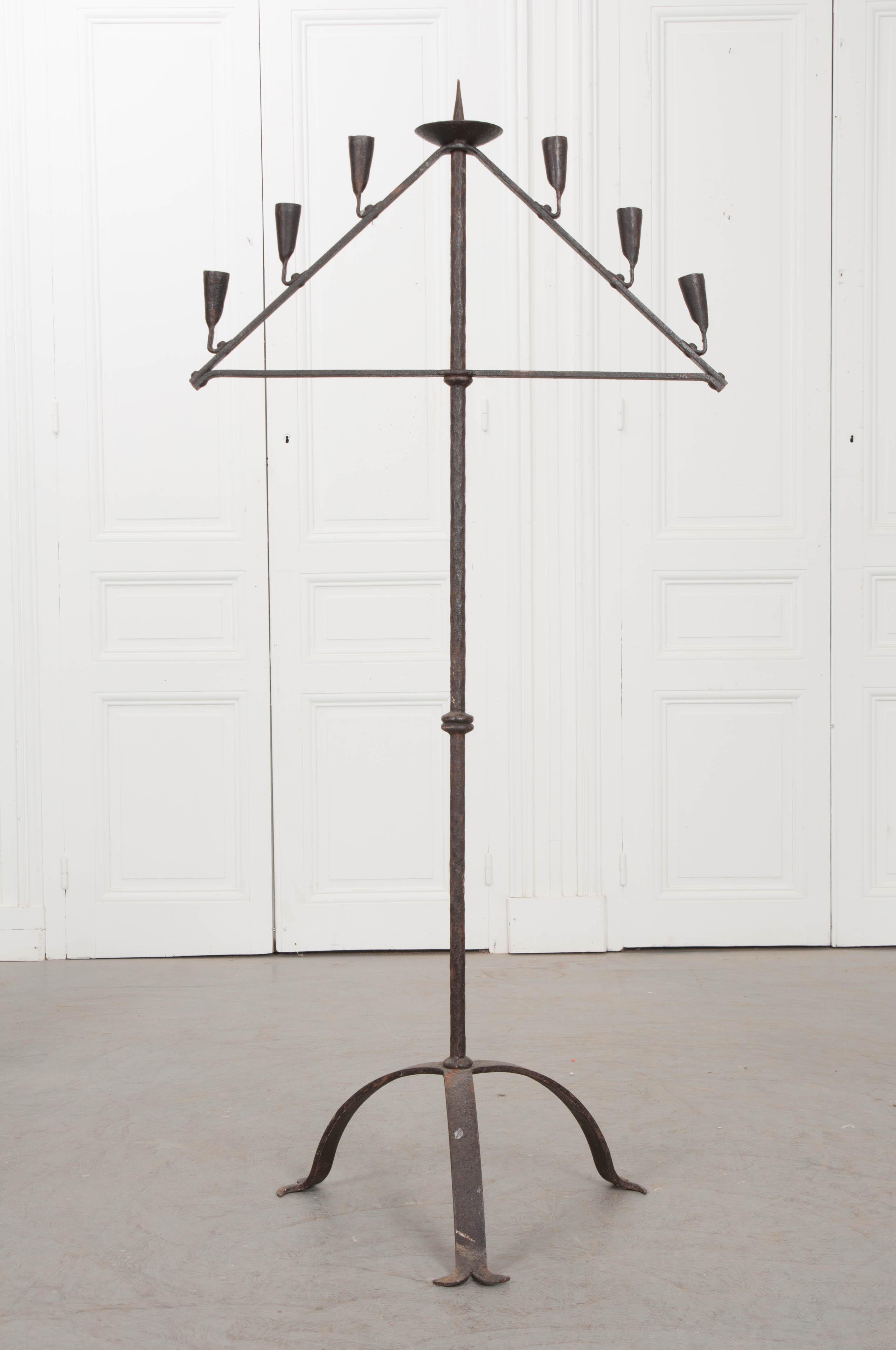 A spectacular hand-forged iron candelabra, made in England circa 1700. The fixture will hold seven candles, arranged in a triangular fashion. Sourced from an English church, the antique fixture has an outspoken Gothic aura that brings the din of