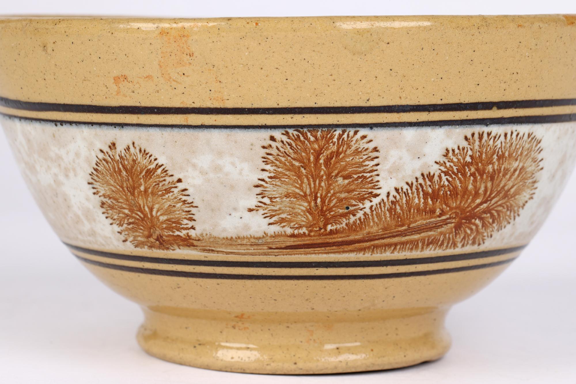 A good and highly collectable antique mocha ware earthenware pottery bowl the body decorated with a band with black slip border and a white slip ground with brown brushed landscape patterns in typical mochaware style dating to the early 19th