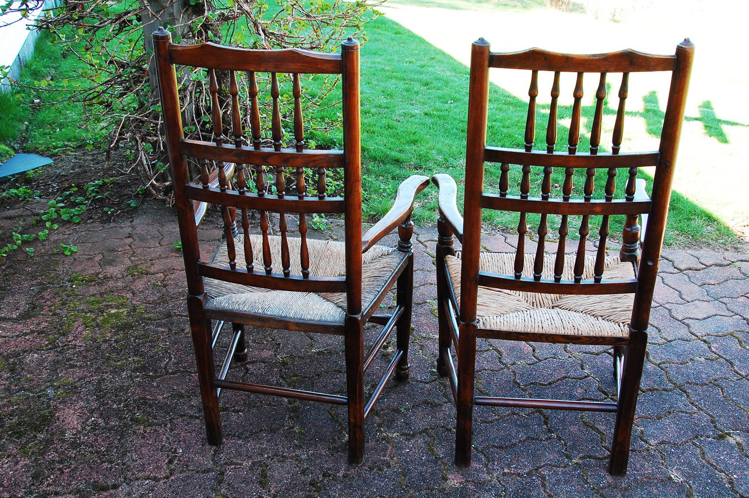 English early 19th century matched pair of spindleback armchairs in elm with rush seats. These hand turned armchairs are from the Lancashire or Cheshire districts of England. Most often these are used as armchairs for a set of dining chairs, but