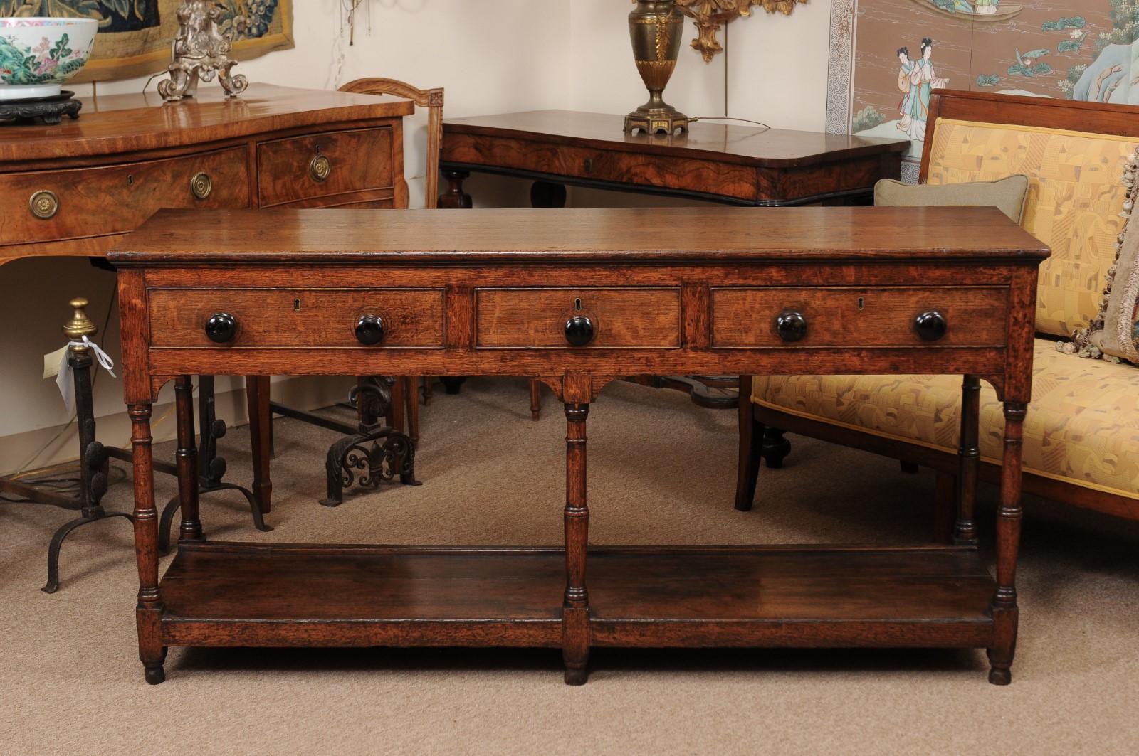 An early 19th century English oak dresser base featuring 3 drawers with round wooden pulls, turned legs joined by lower plinth ending in rounded feet. 

 
