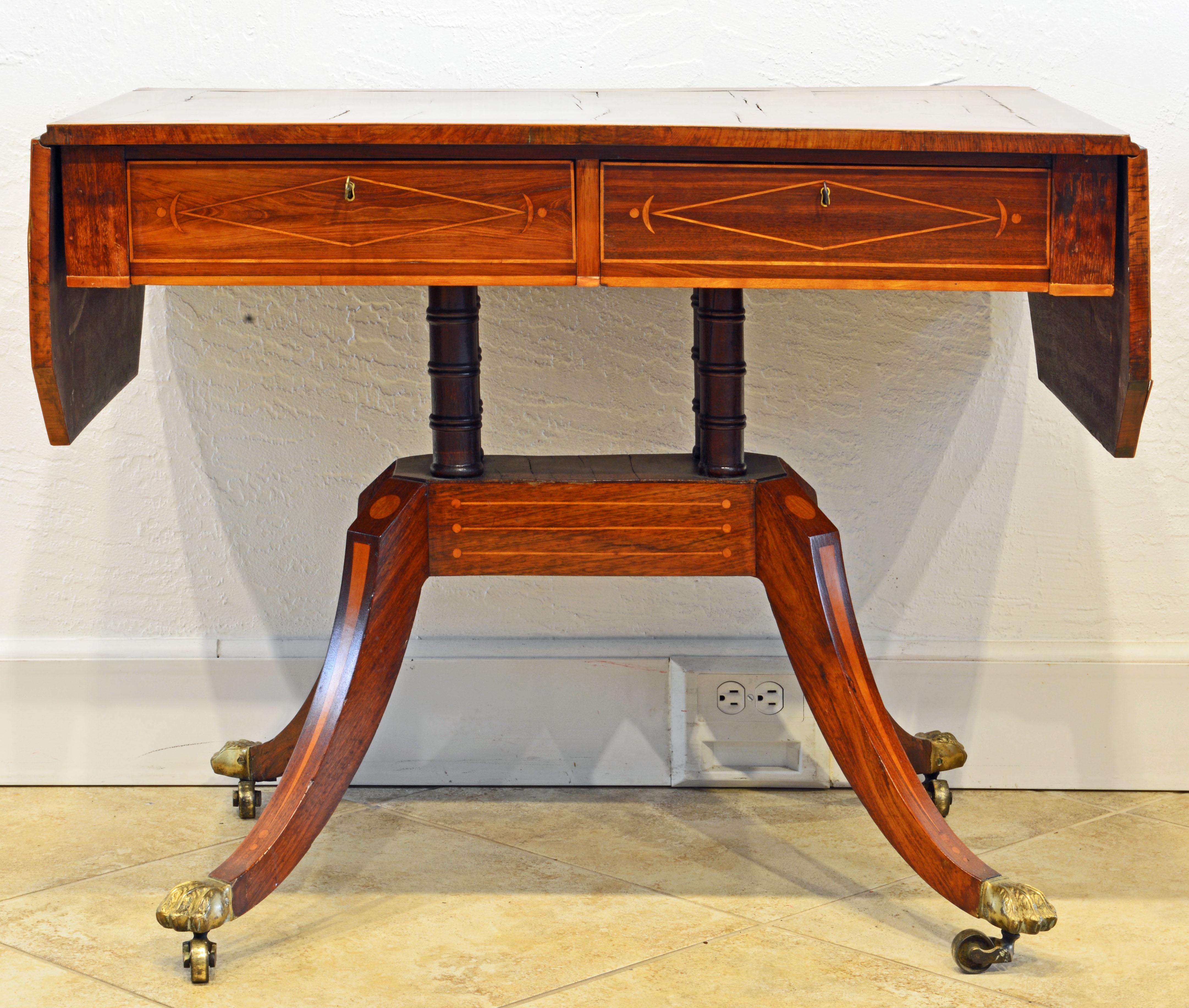 This early regency rosewood sofa table features satinwood inlay with stars, spheres and moons on the banded top, drawer fronts and base. The other side has simulated drawers identical with the front. The table rests on four turned columns connecting