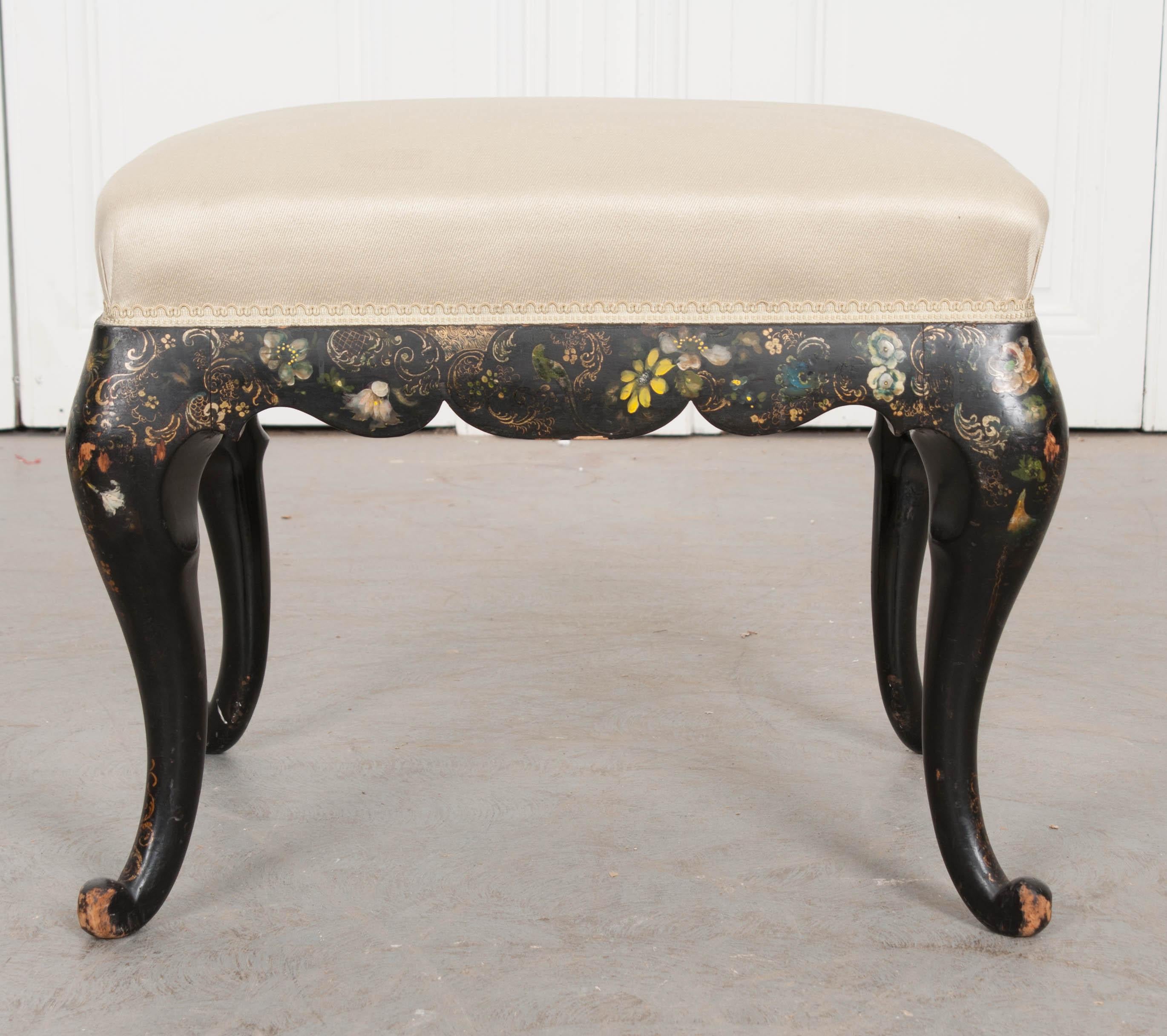 A beautiful hand painted stool from 1900s, England. The antique is upholstered in a creamy gold silk fabric that is affixed to the frame using the same creamy gold-colored gimp tape. The frame is ebonized, with the four legs having a cabriole form