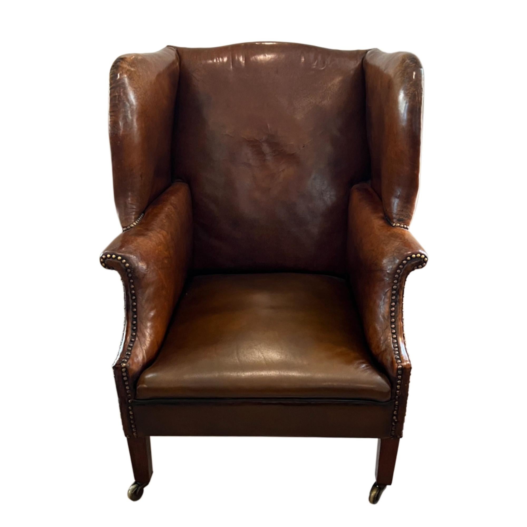 This extremely comfortable leather wing chair was made in England in the early 20th century. Beautifully constructed with a rich brown leather, brass studs and mahogany legs. The front feet are finished with the original brass castors - please take