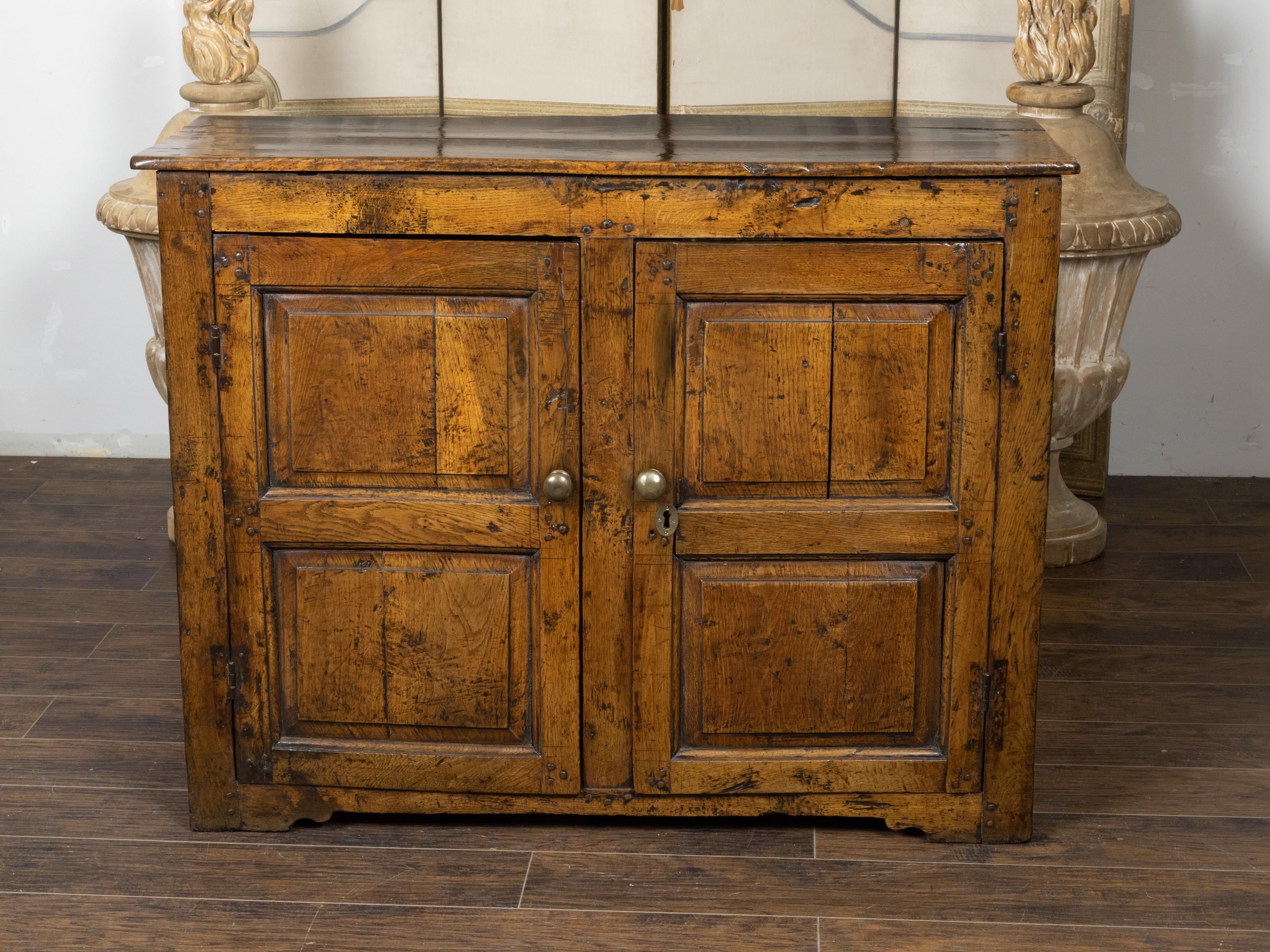 Une armoire anglaise en chêne du XVIIIe siècle, d'aspect rustique, avec deux portes, des panneaux sculptés et une patine d'ancienneté. Créée en Angleterre au XVIIIe siècle, cette armoire en chêne nous séduit par son côté champêtre et ses lignes