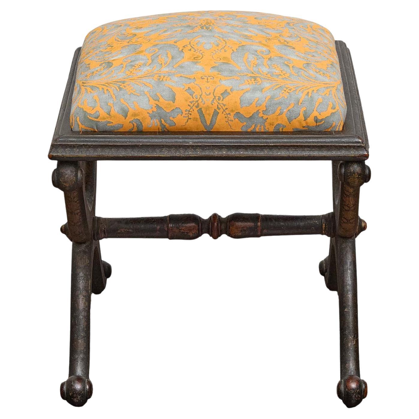 An English ebonized stool from the 19th century, distinguished by its curving X-form base and elegant hand-painted decoration in the chinoiserie style. The sinuous legs form graceful arcs at each side, joined by a turned stretcher and finished in