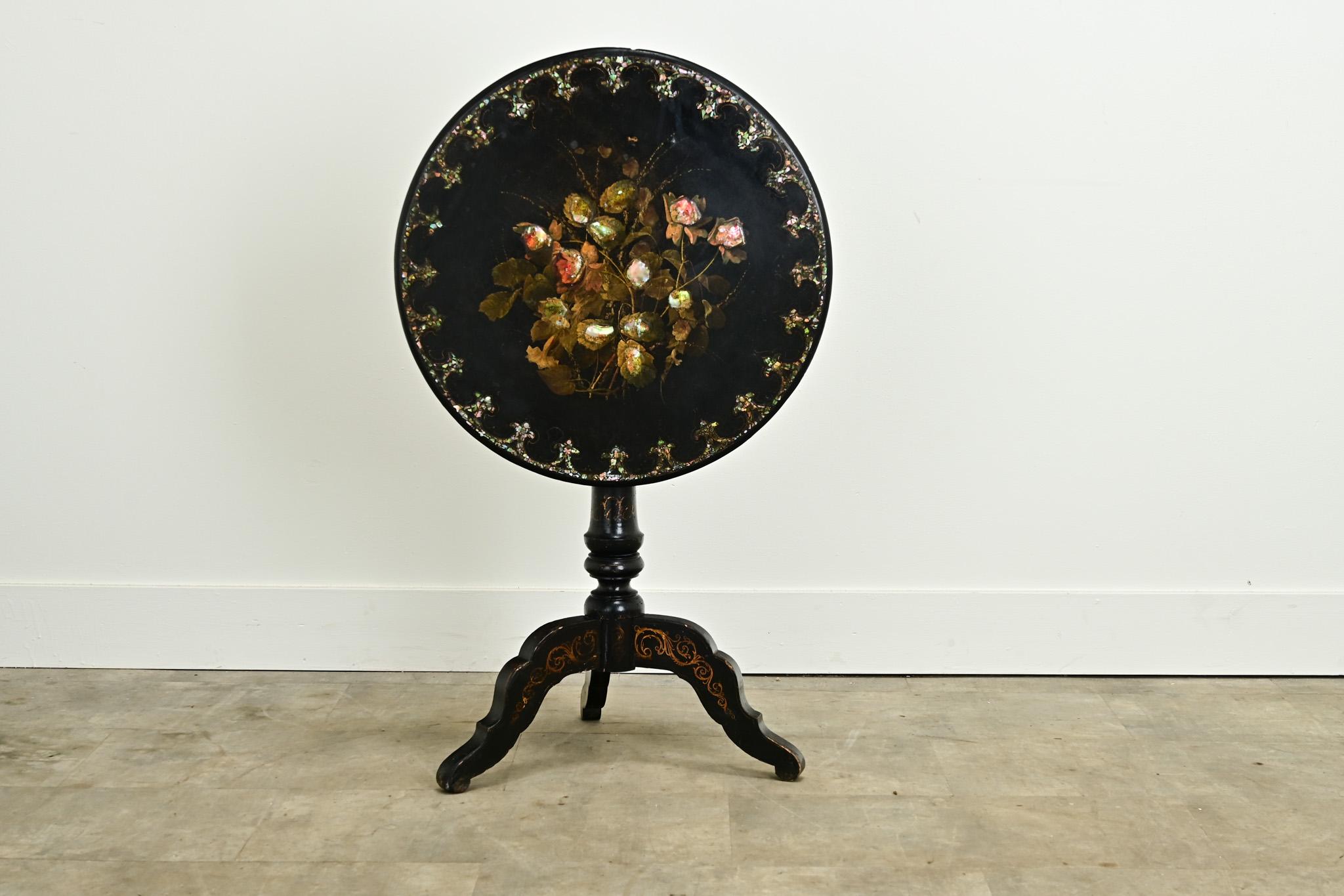 This impressive English ebonized and inlaid tilt top tea table will make a statement in any interior. This table is ebonized and has inlay of mother-of-pearl and paper mache painted flowers. The top sits on a splayed pedestal base with hand painted