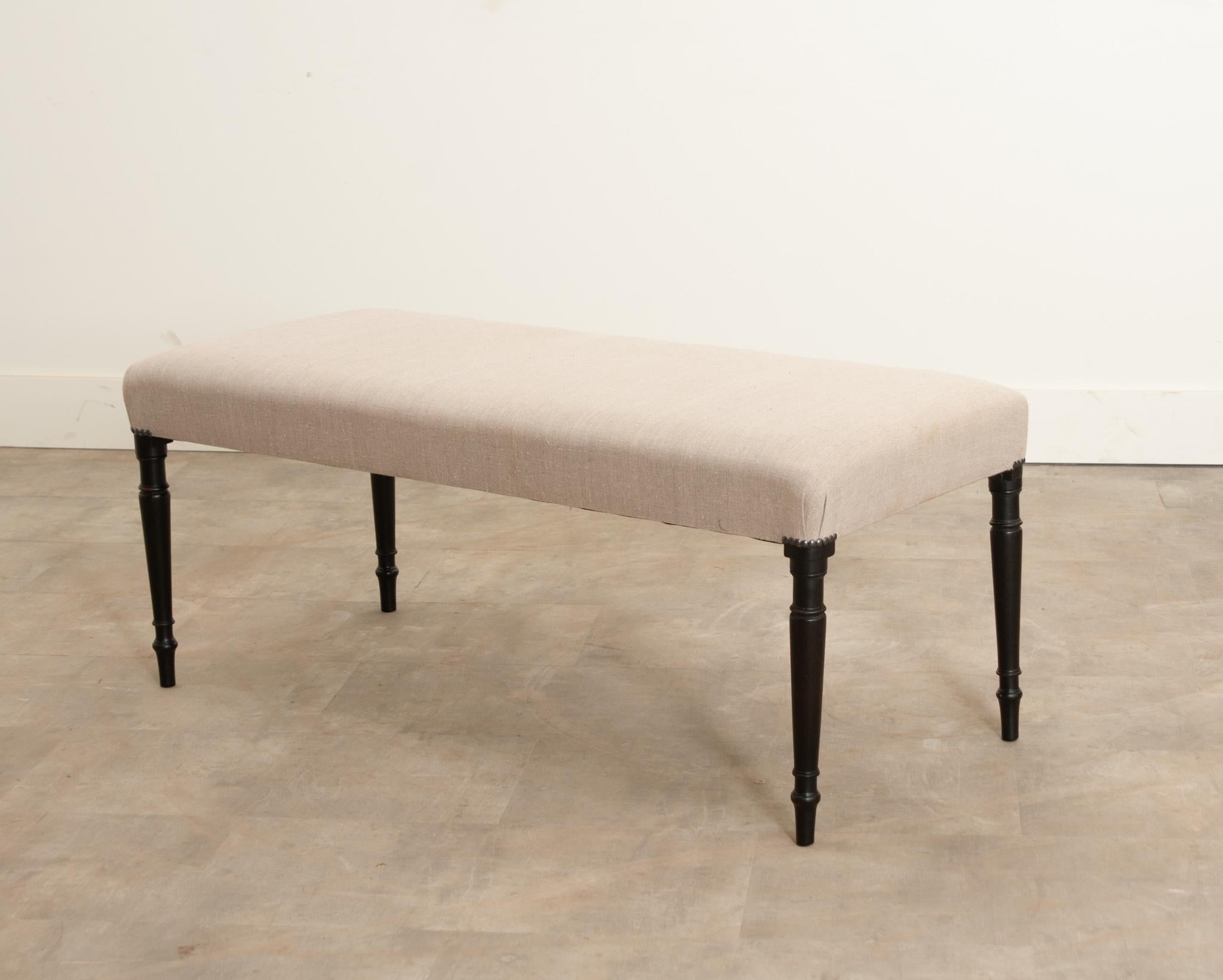 A lovely little bench from 19th century England that goes perfectly with any decor style. Recently upholstered with a wonderful neutral fabric that's fixed to the frame with simple round nail heads. Sleekly turned, ebonized legs support the whole.