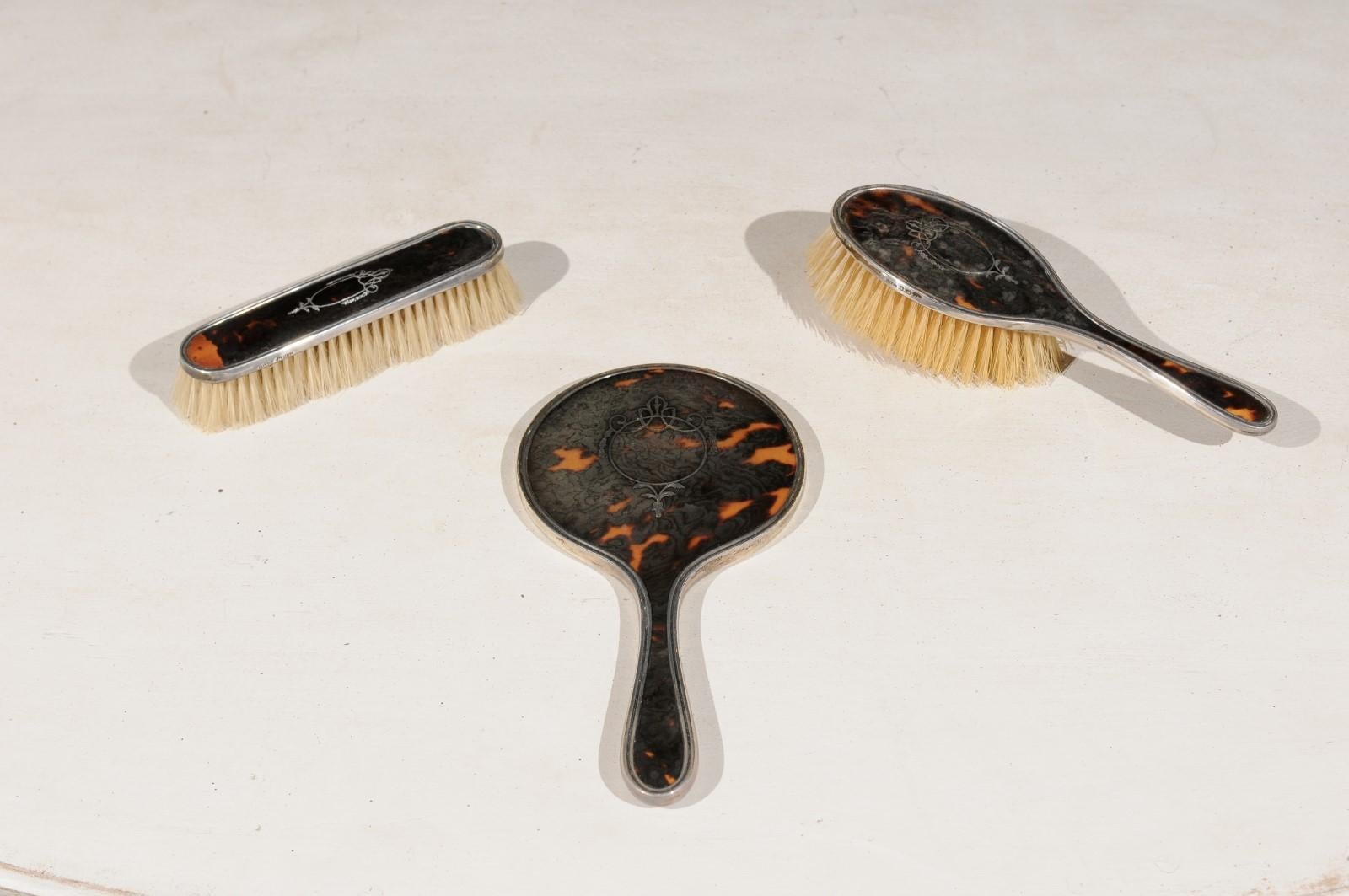 An English Edwardian period dressing table hand mirror, hair and clothes brushes from the early 20th century with silver piqué décor of garlands and medallions. Born in England during the early years of the 20th century, this exquisite set of hand