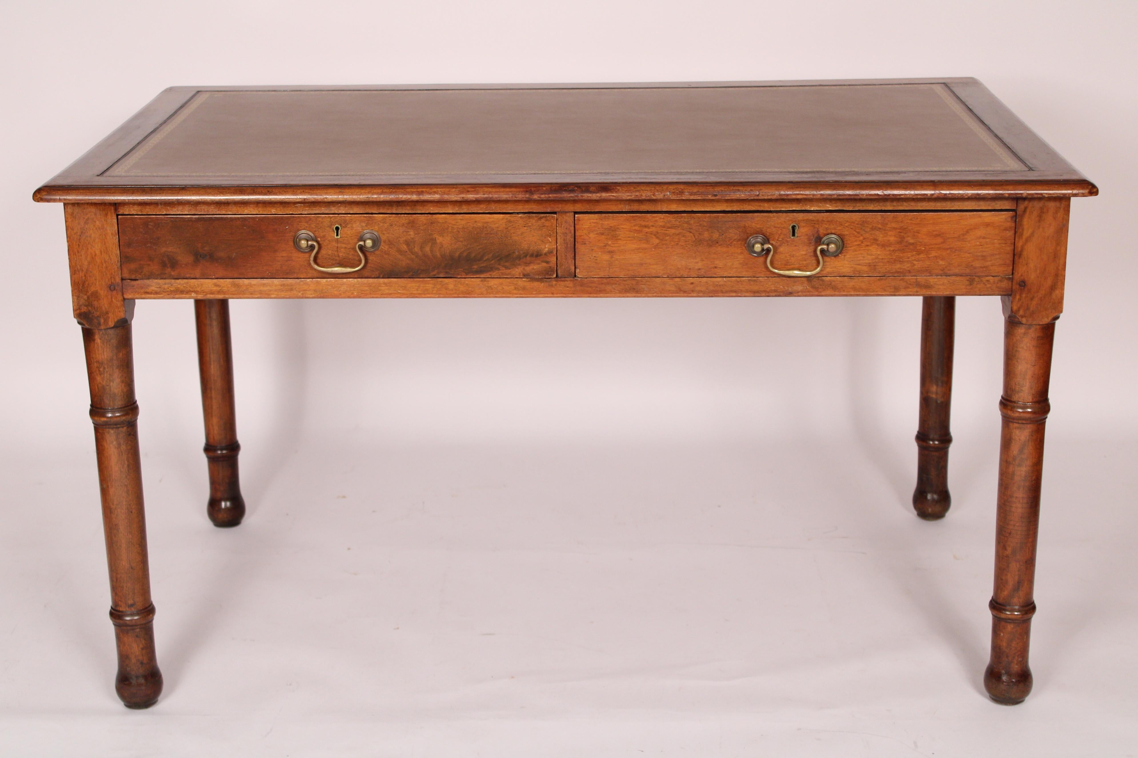 English Edwardian beech wood writing table with a tooled leather top, circa 1910. With an overhanging thumb molded top inset with tooled leather, two frieze drawers with brass pulls, resting on bamboo style turned legs. Knee clearance 24