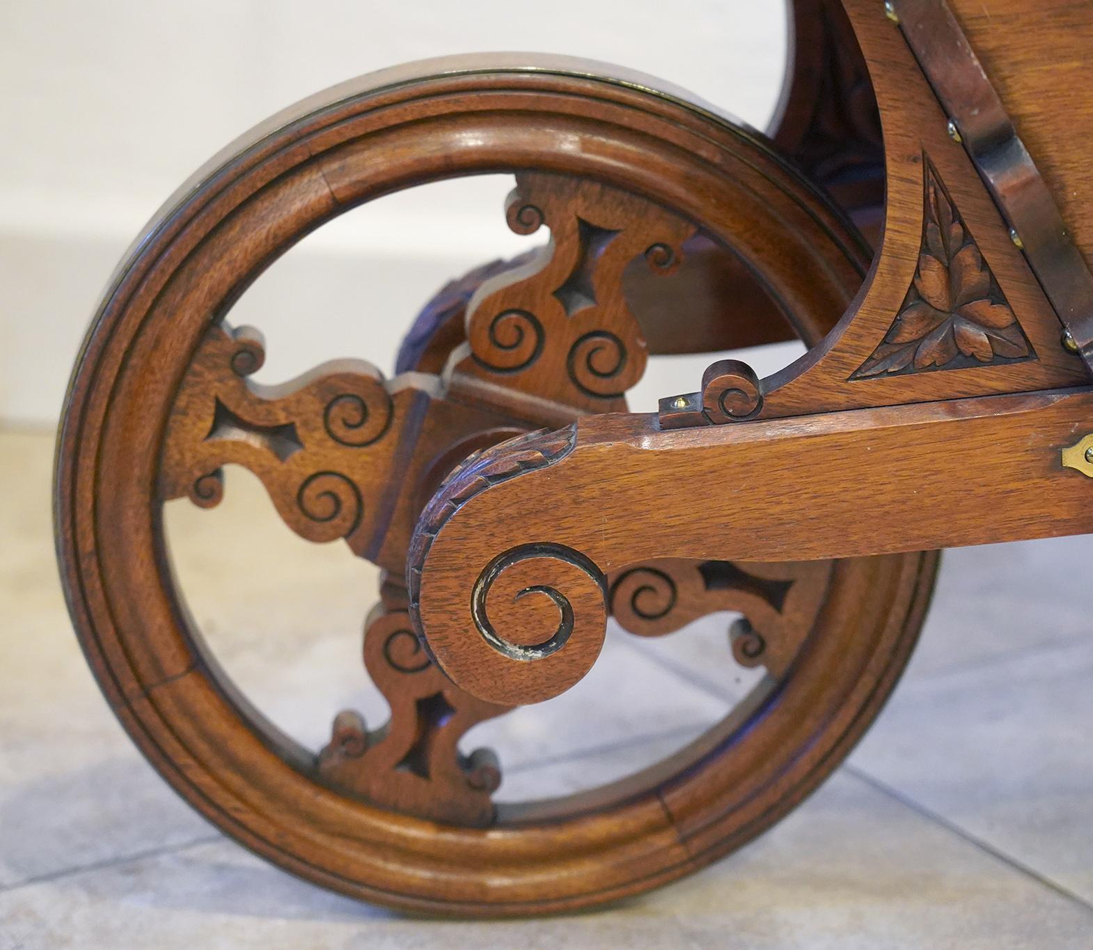 This early 20th century English Edwardian carved mahogany wheel barrow was used for the transport and display of books in a library setting. It is artfully crafted with brass-clad wheel and decorative brass hardware, carvings and turned axel. It